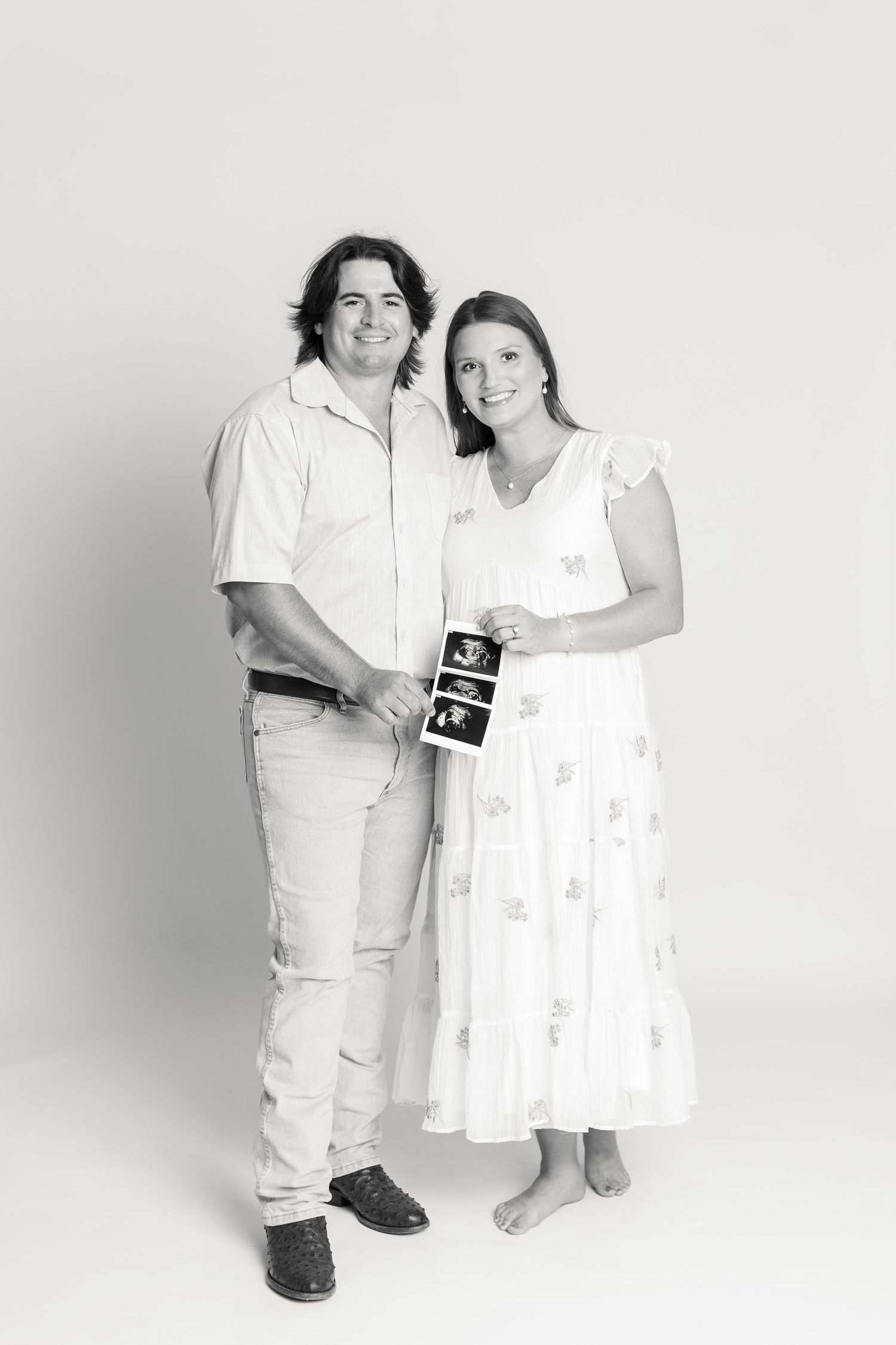 Happy couple smiling and holding ultrasound photos in a black and white maternity portrait studio photo.