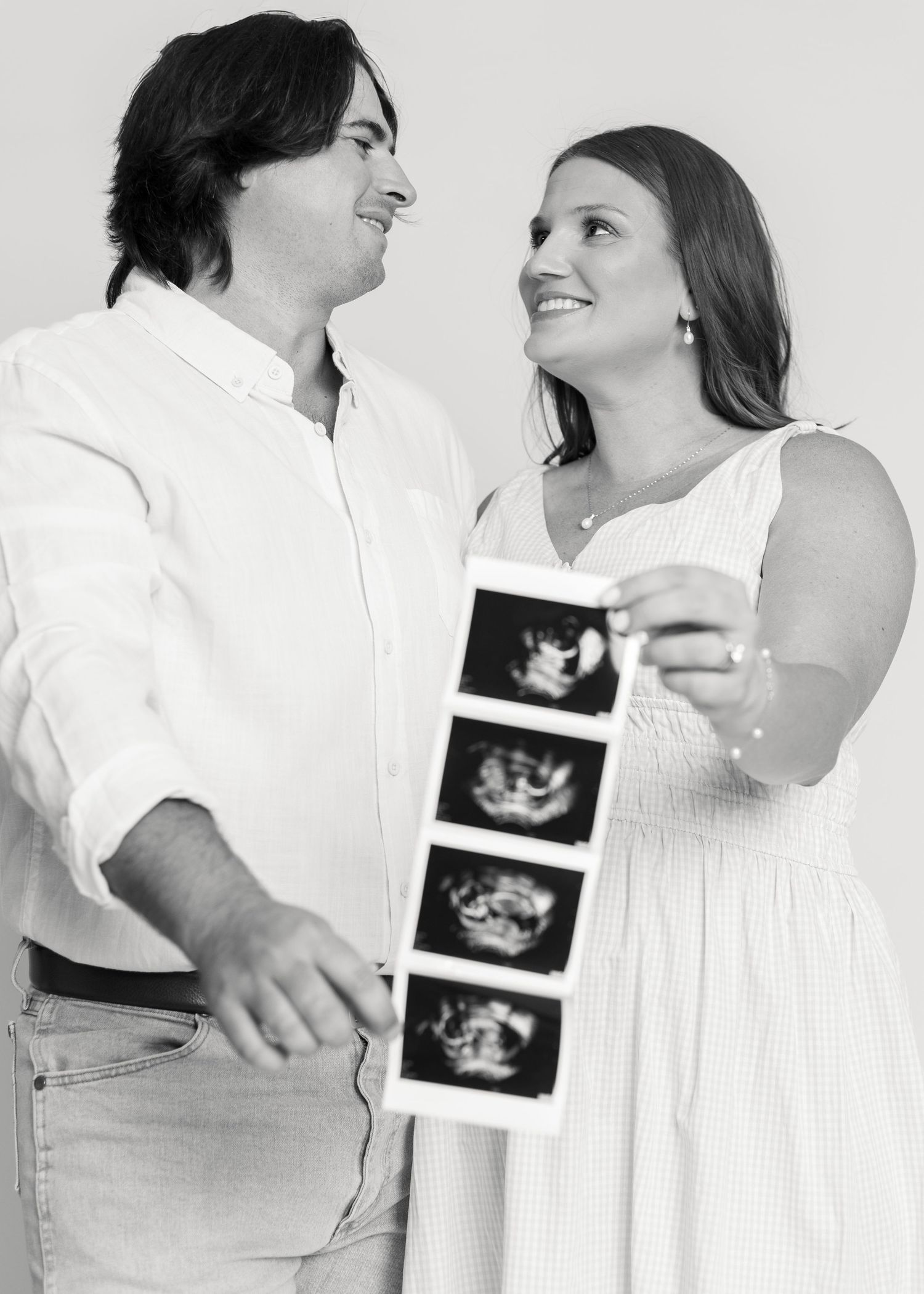 Black and white photo of a smiling couple holding ultrasound images, announcing their pregnancy.
