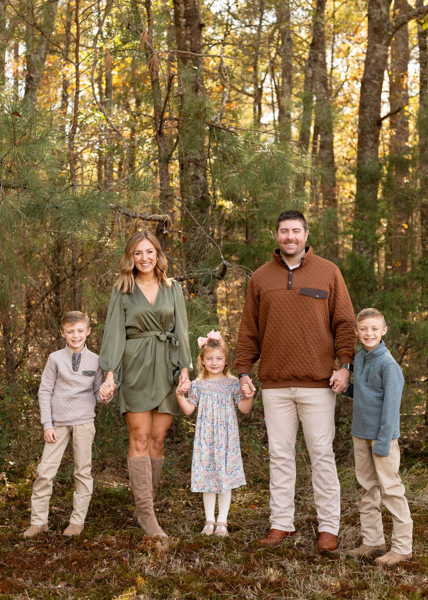 A family of five poses in an autumn forest, parents holding hands with three children in coordinated fall outfits.