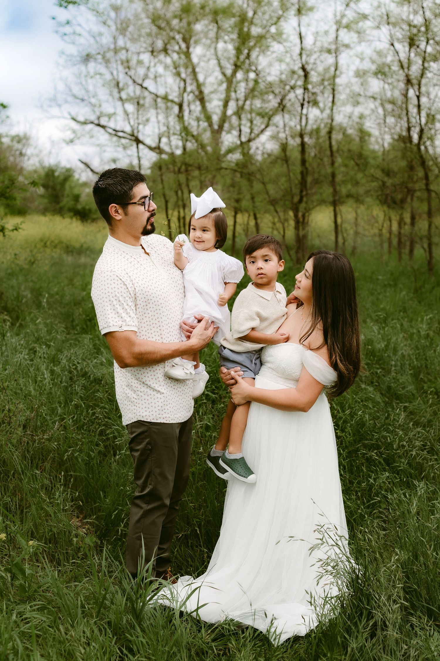 A family stands together in a grassy field with trees in the background on a spring day.