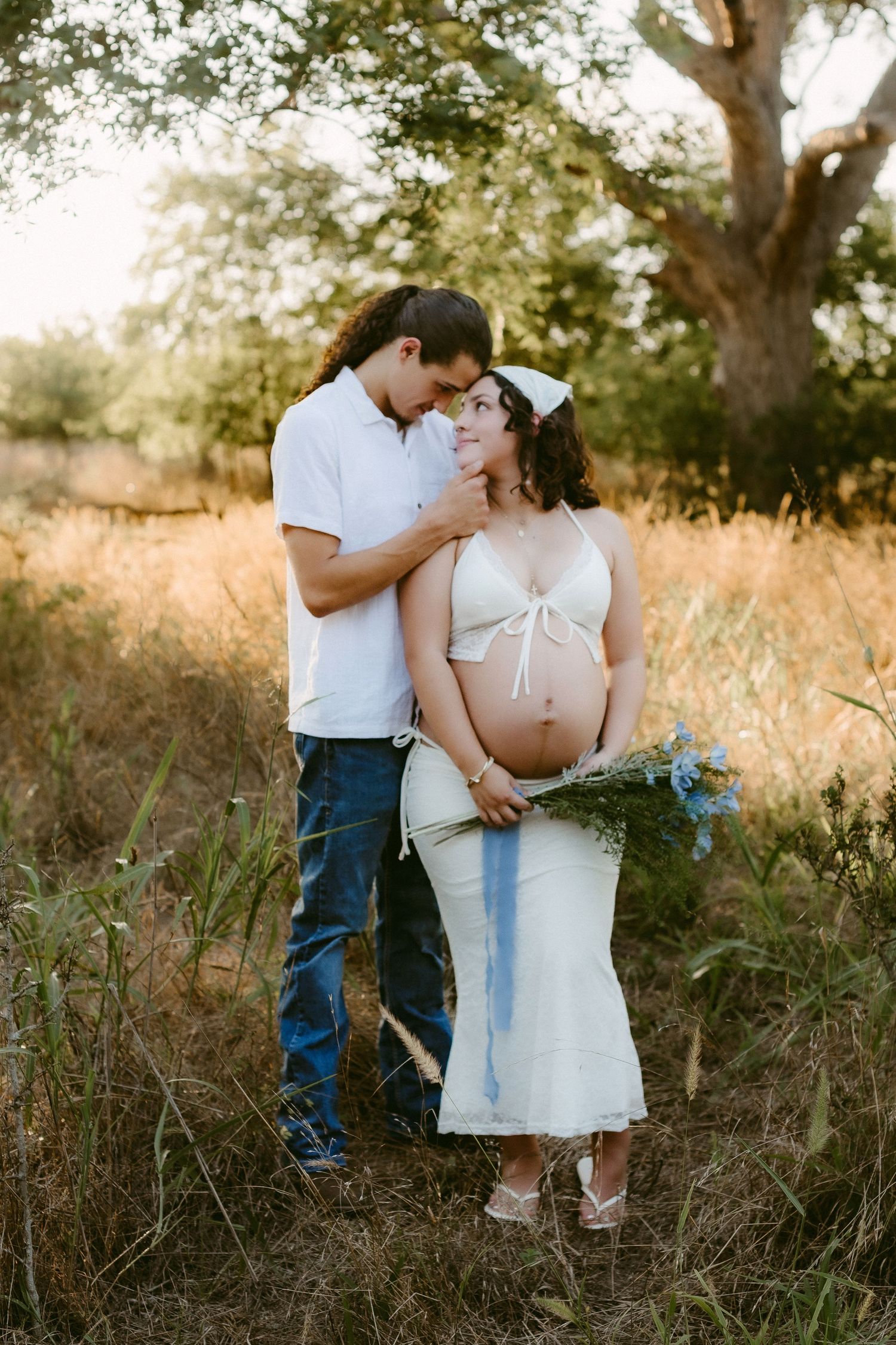 Romantic maternity portrait in a sun-drenched field with trees.