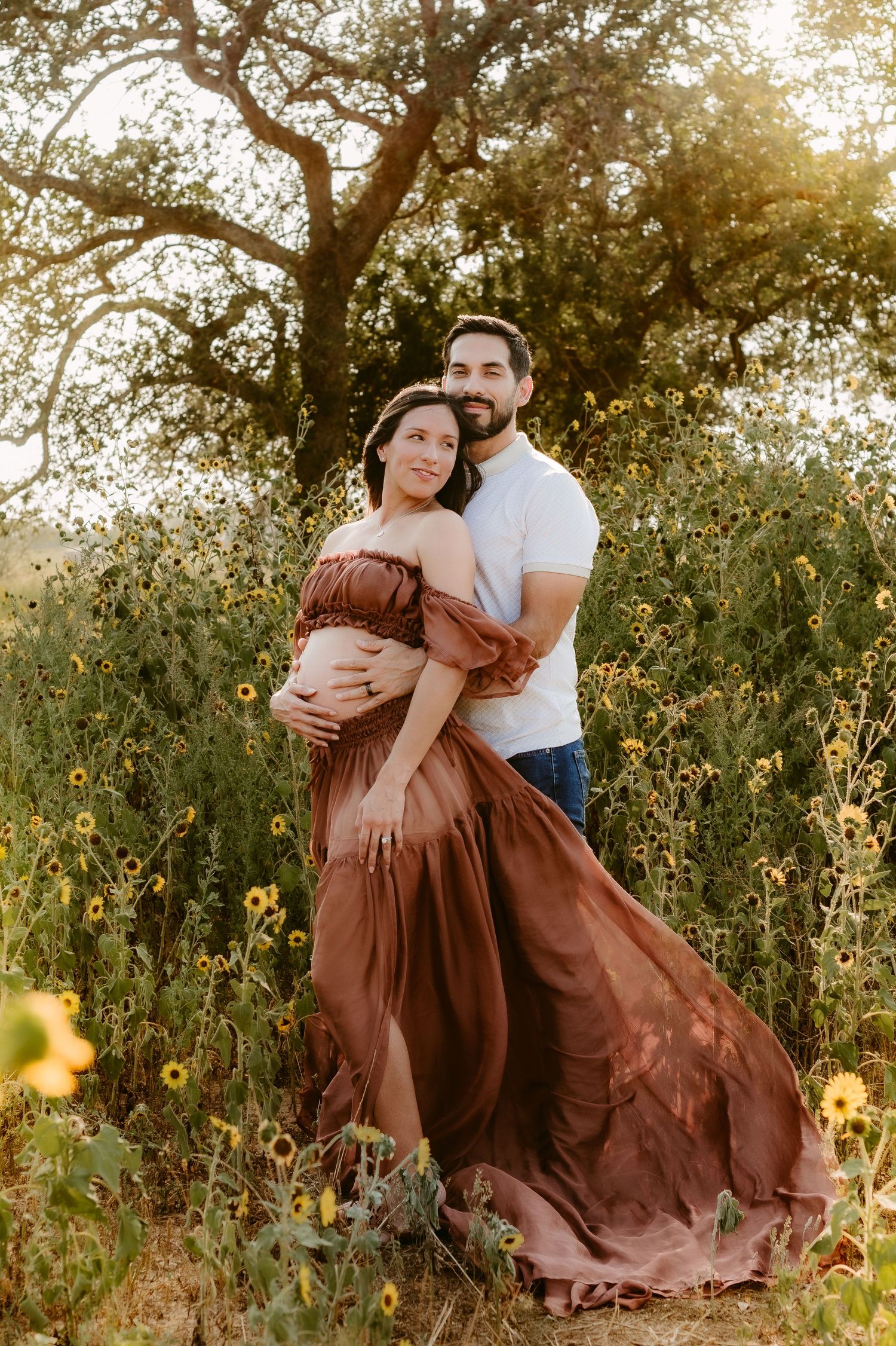 A couple embraces in a romantic outdoor setting with golden sunlight filtering through trees behind them in nature.