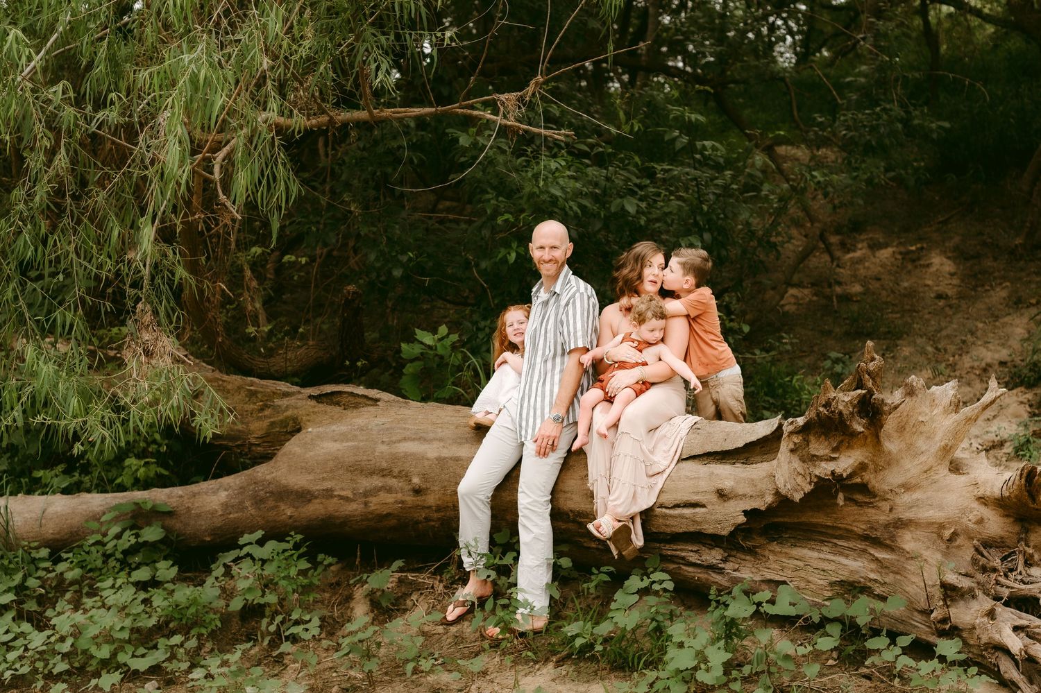A family sits together on a fallen log in a lush green forest setting.