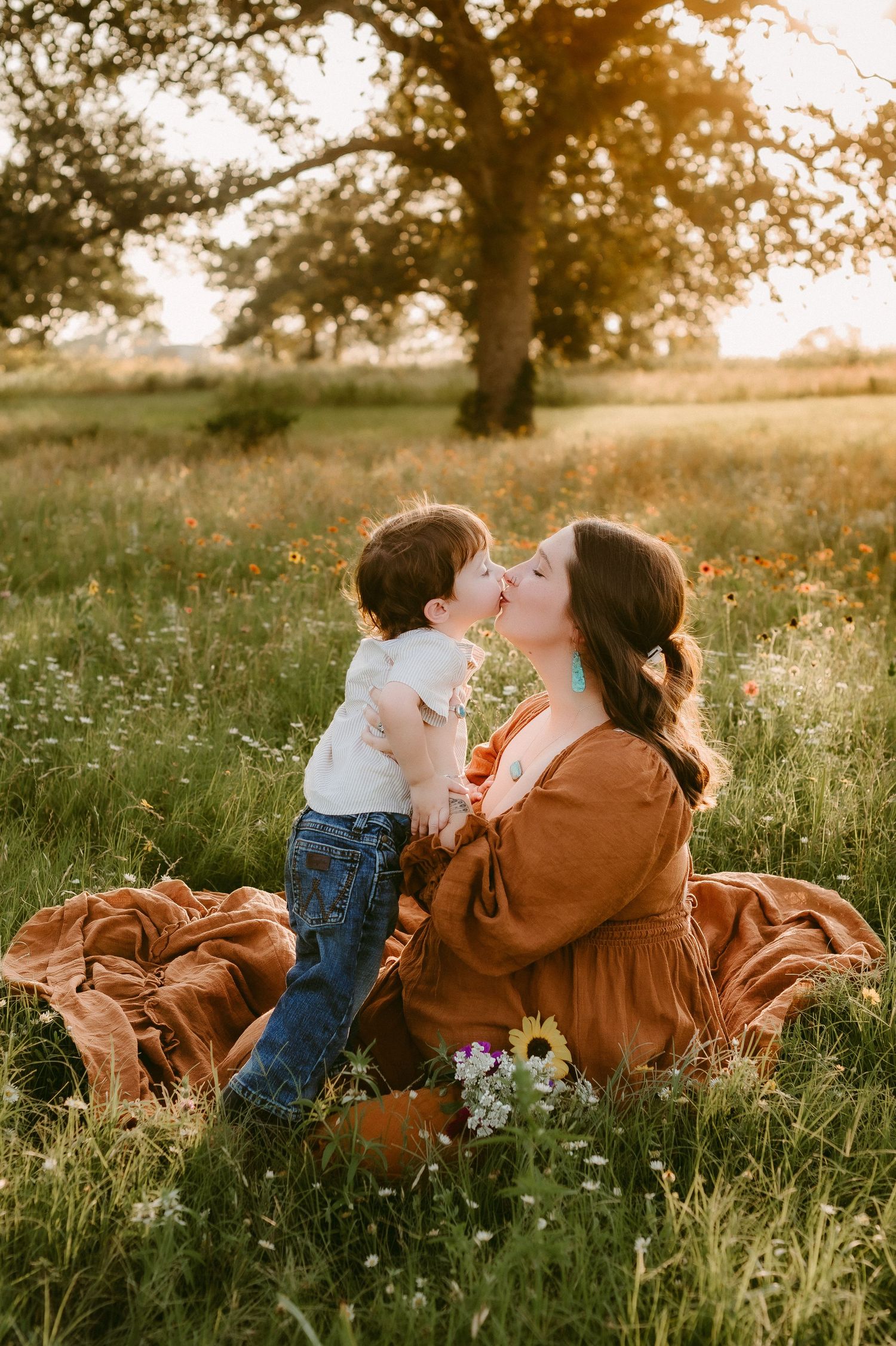 Mother and child share tender moment in sunny meadow with wildflowers at golden hour.