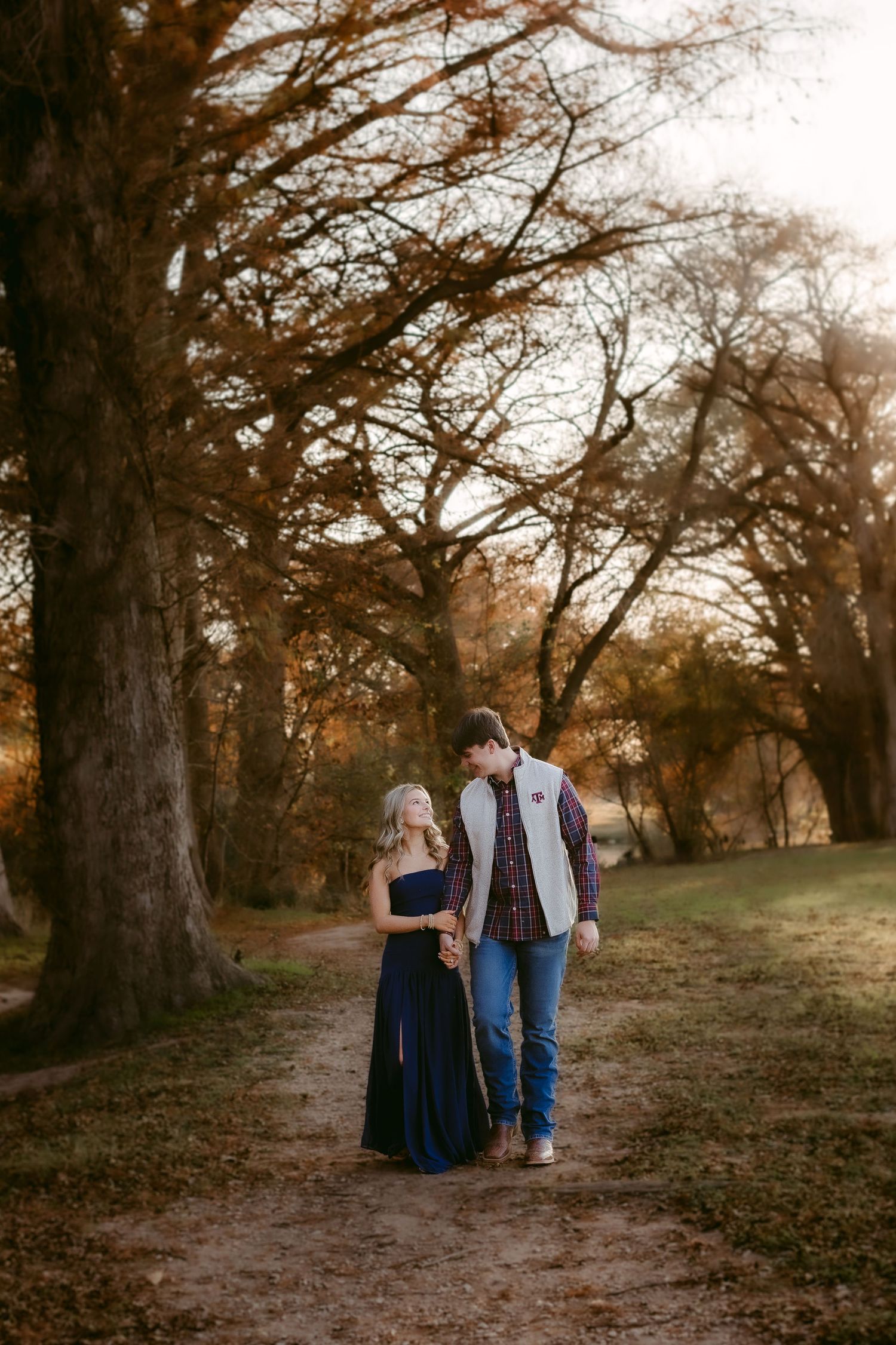Couple strolling down a romantic autumn path lined with tall trees at sunset in a park.