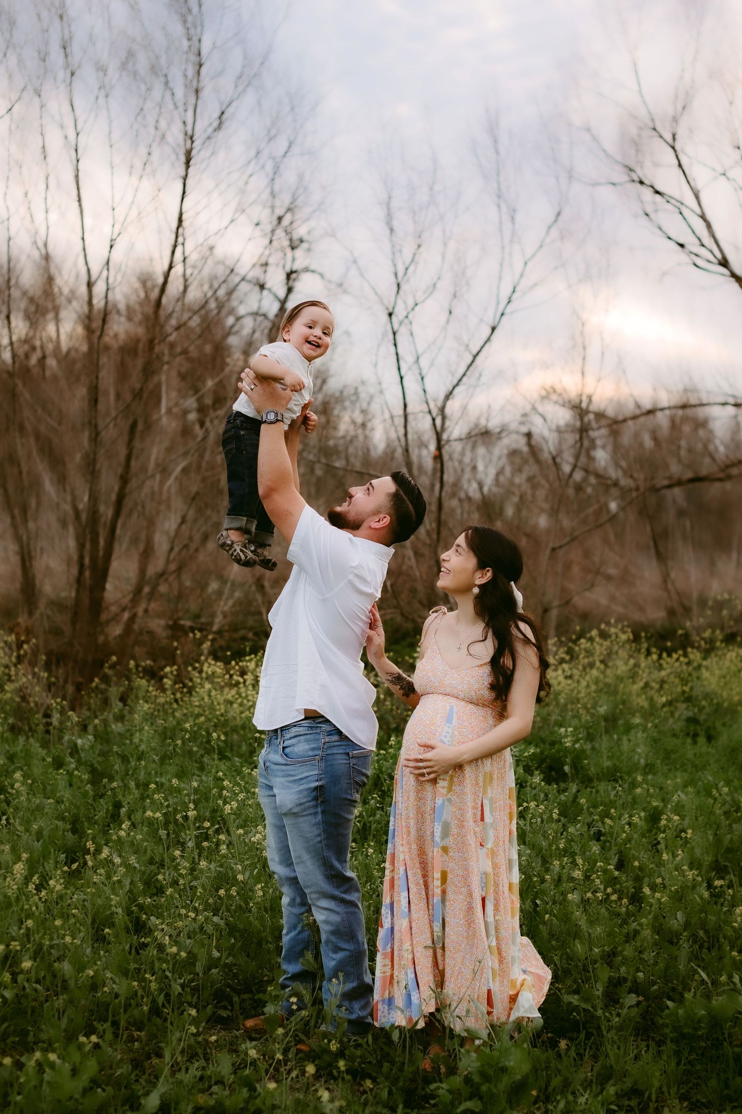 A family stands together in a wildflower meadow at dusk with bare trees in the background.