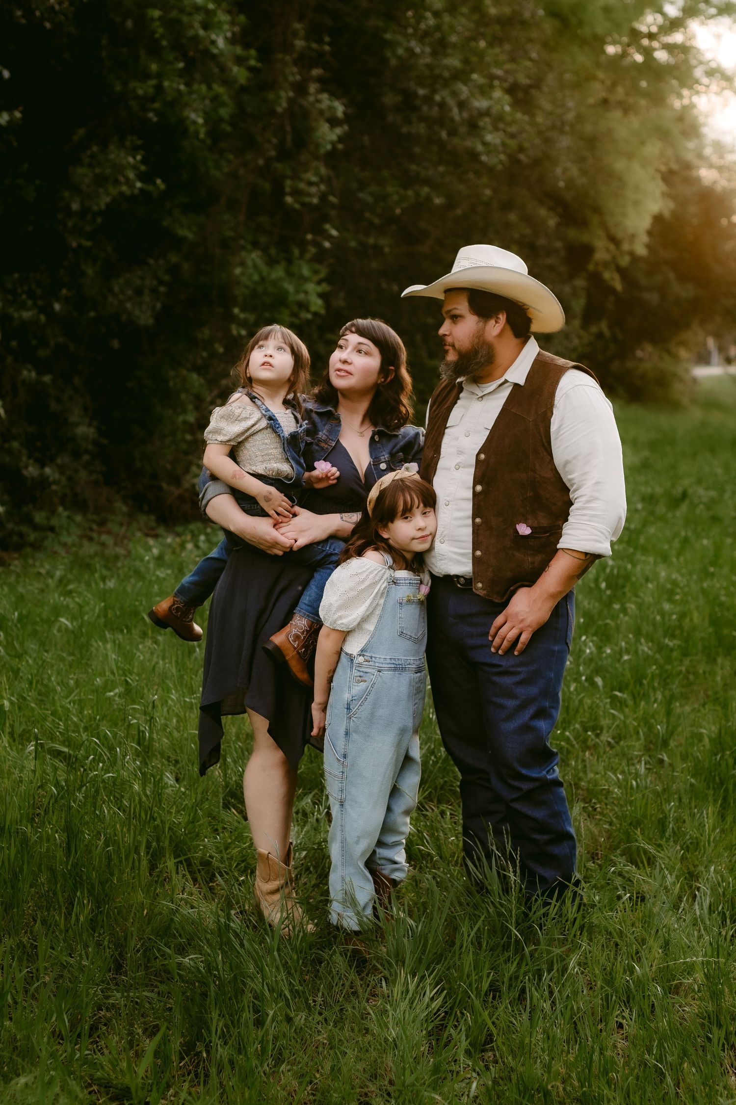 Family in vintage-style clothing poses together in sunlit grassy field.