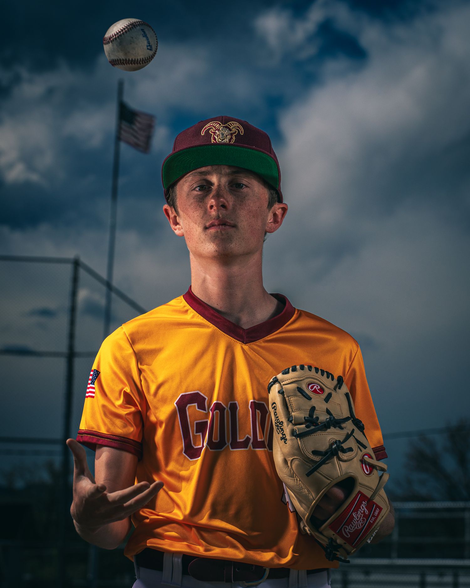 Baseball player in yellow jersey assumes pitching stance on field during cloudy dramatic weather conditions.