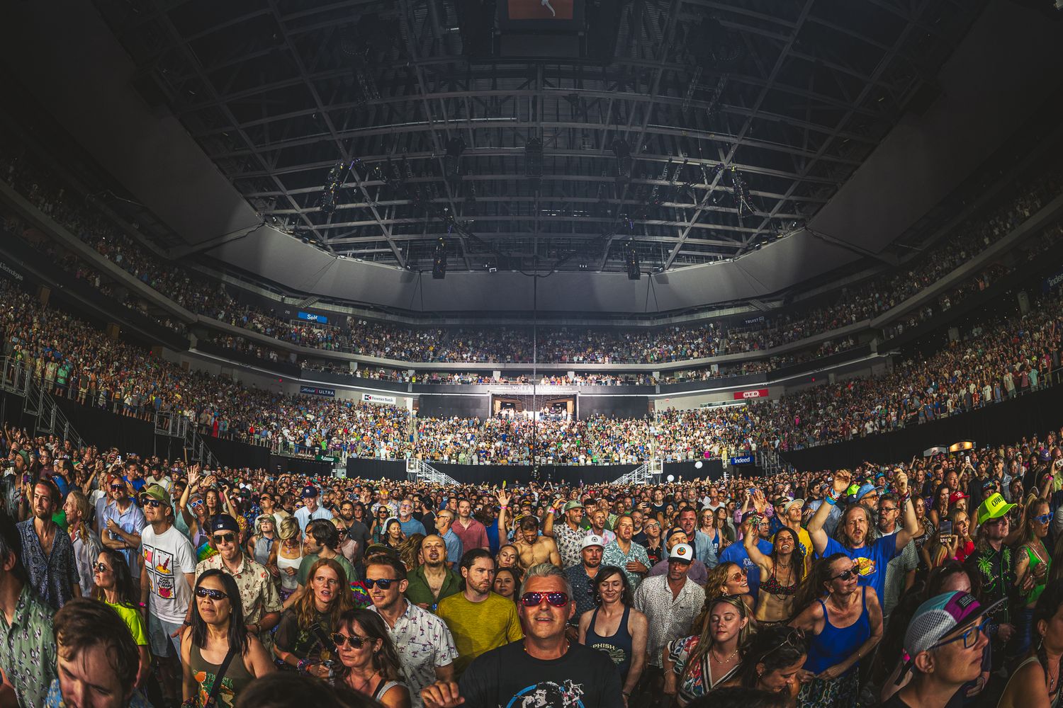Large crowd of concert attendees fills arena floor and seating during live performance with dramatic lighting and high ceiling.