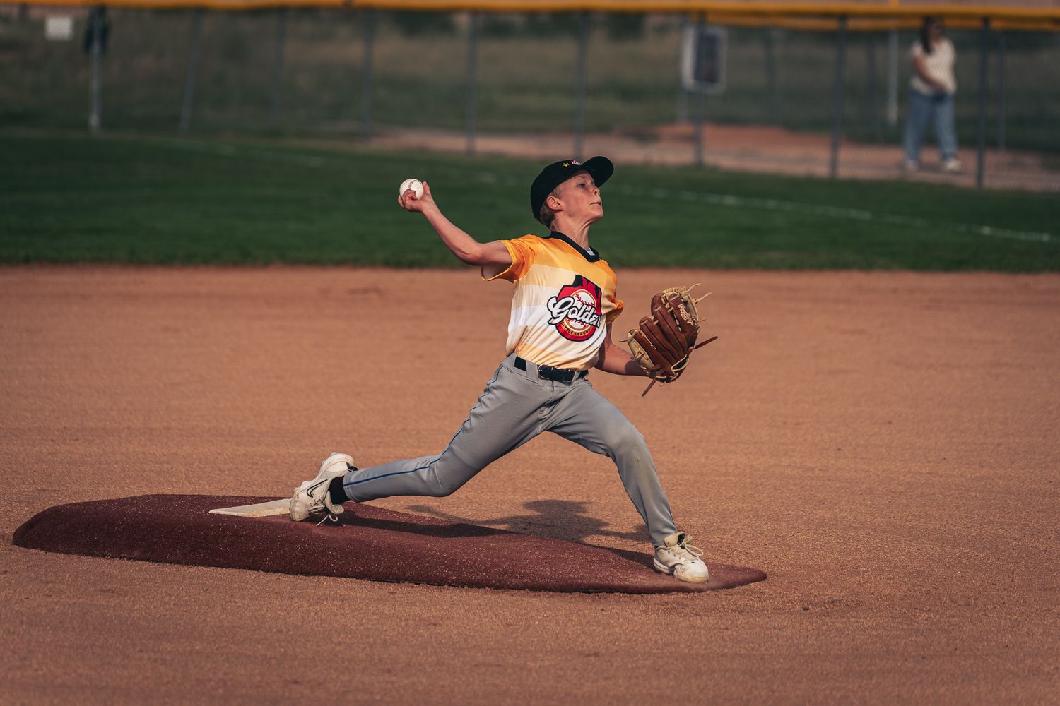 Baseball pitcher follows through on delivery motion during game on dirt infield.
