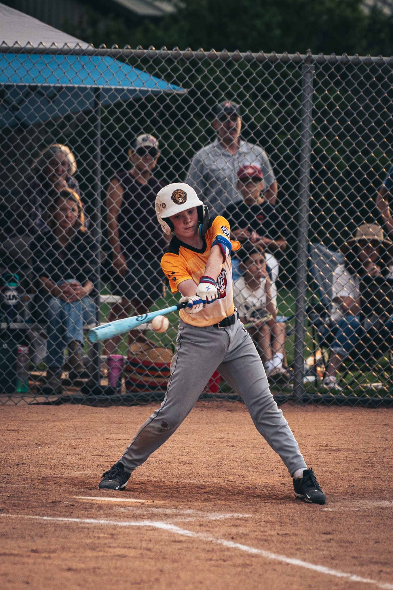 Five sequential frames show a youth baseball player's batting stance and swing during a little league game.