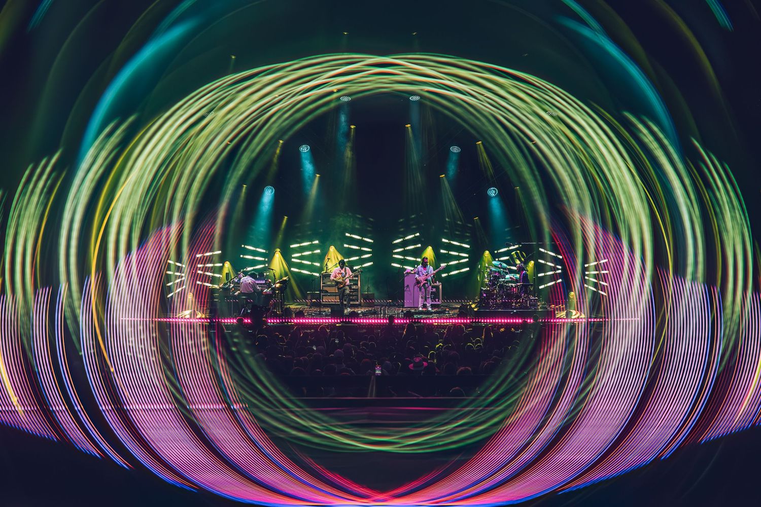 Concert stage illuminated with vibrant neon green, yellow and pink lights creating circular tunnel effect during performance.