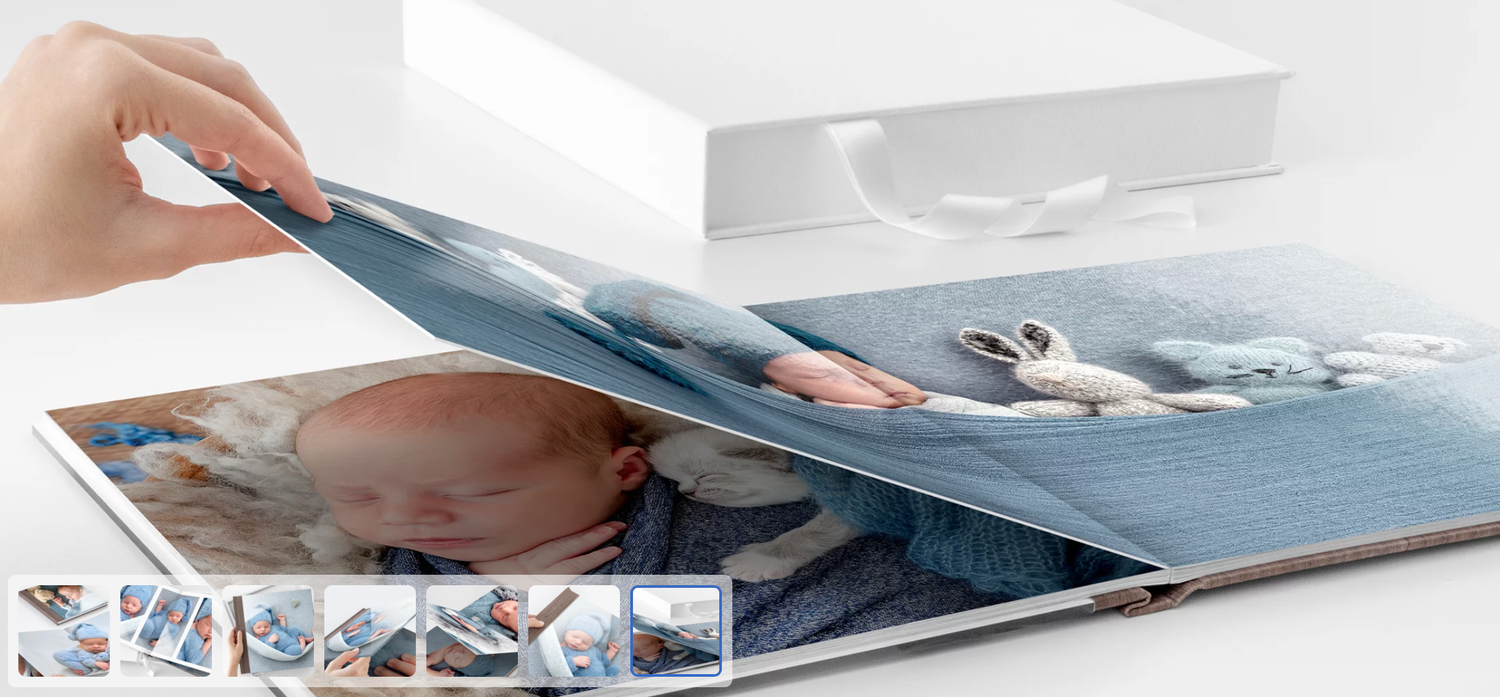 Hand opening a premium hardcover photo book featuring a sleeping baby, with thumbnail previews of additional pages below.