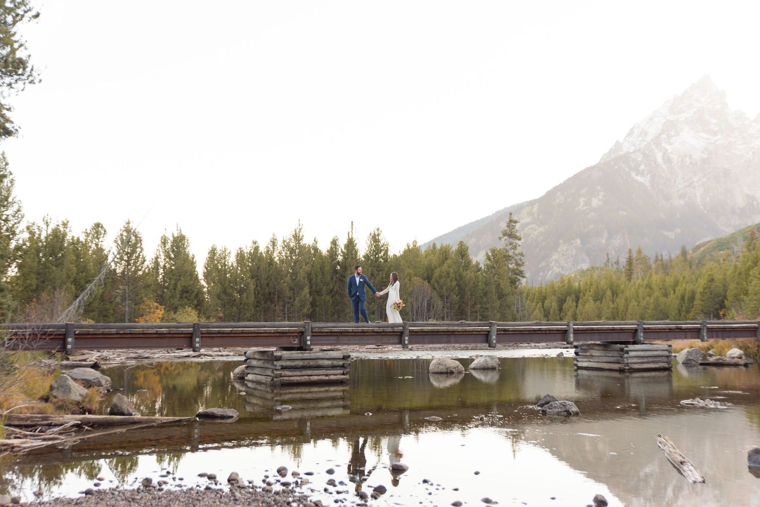 A wooden dock stretches across a serene mountain lake surrounded by evergreen trees.