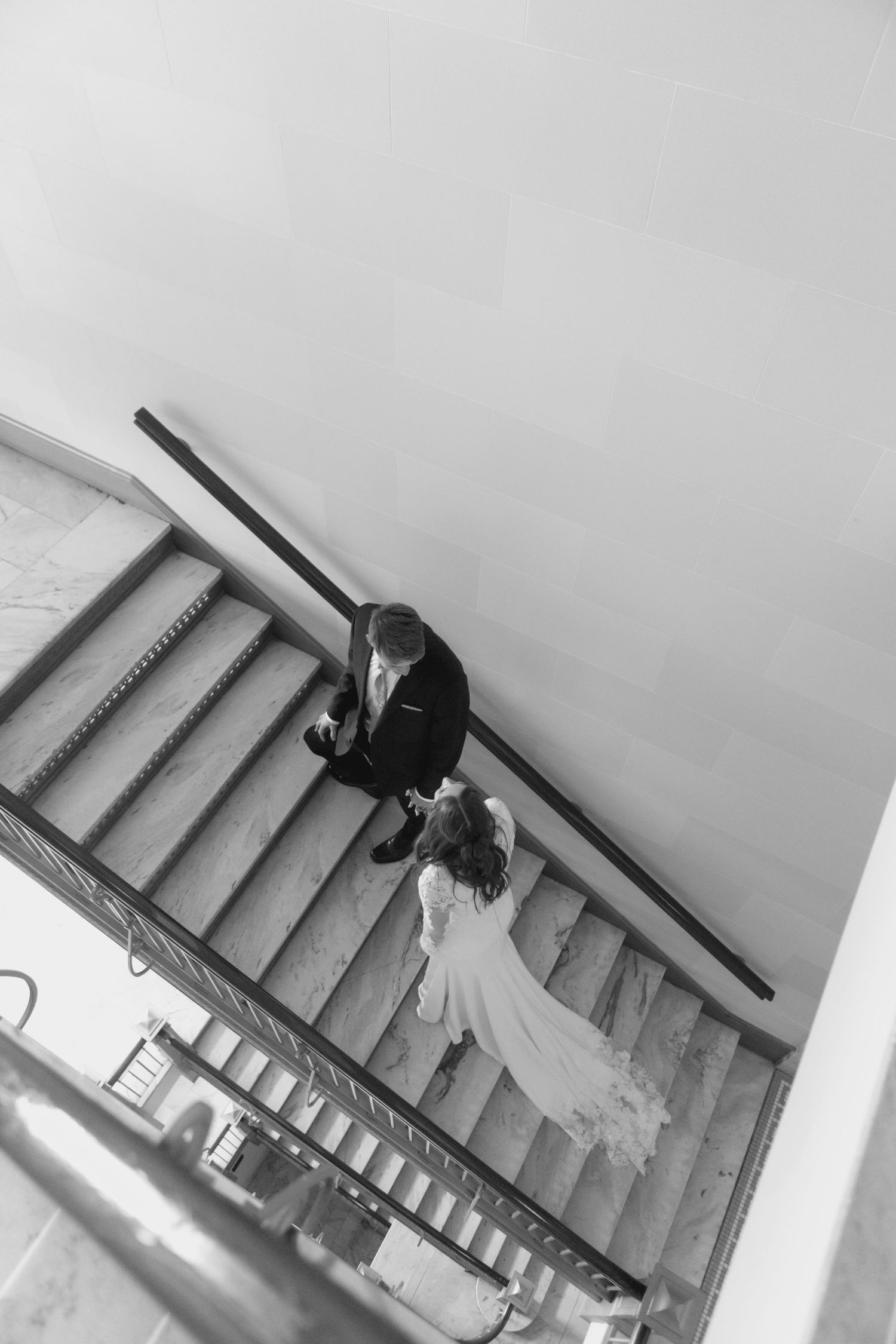 Aerial black and white photo of bride and groom embracing on grand staircase at wedding venue.