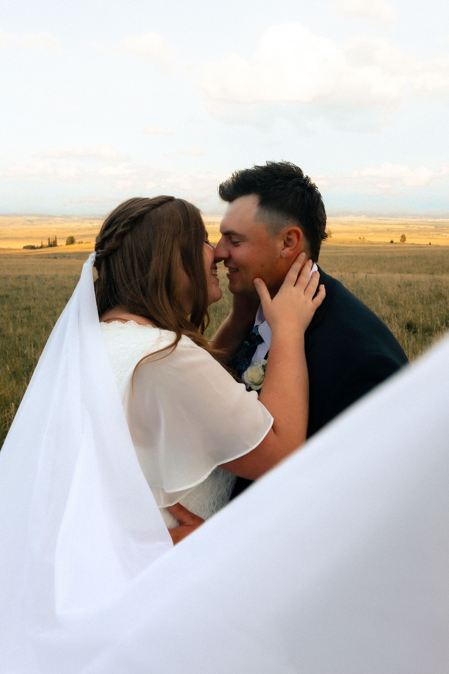 A bride and groom share a romantic moment in a golden field, with her veil flowing in the breeze.