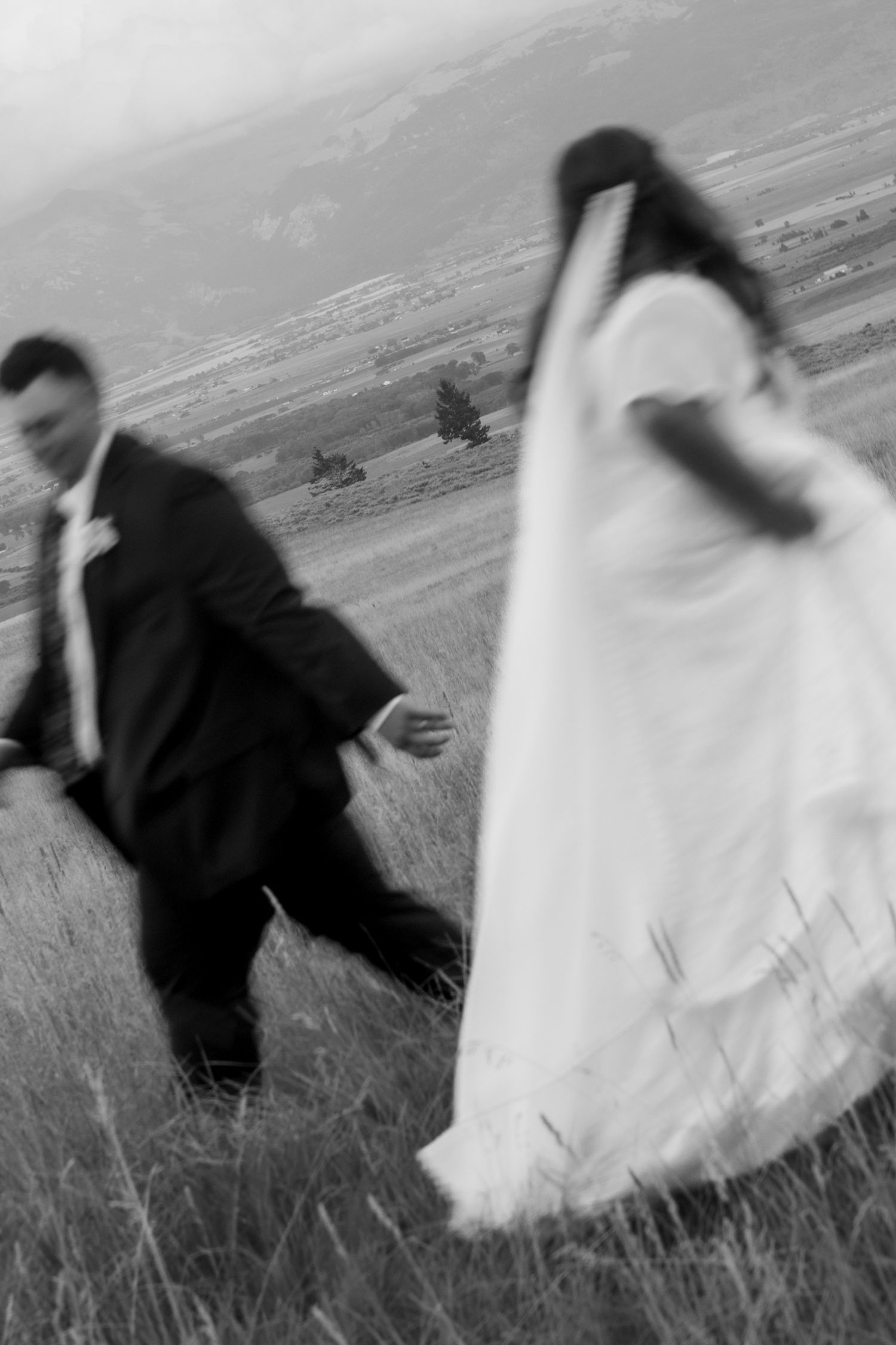 Blurred black and white photo of bride and groom running through a field on their wedding day.