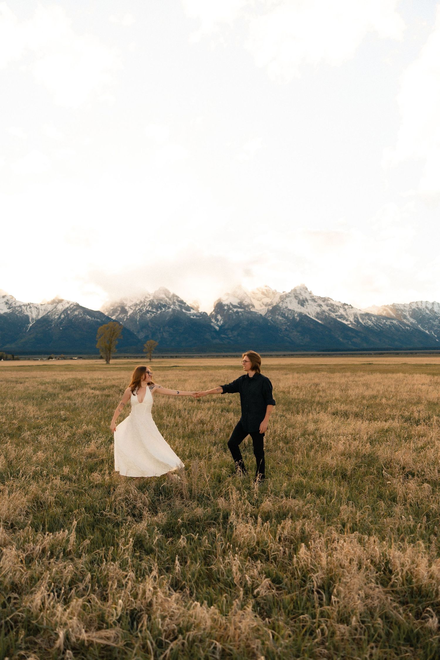 Couple dancing in a golden field with snow-capped Grand Teton mountains in the background.
