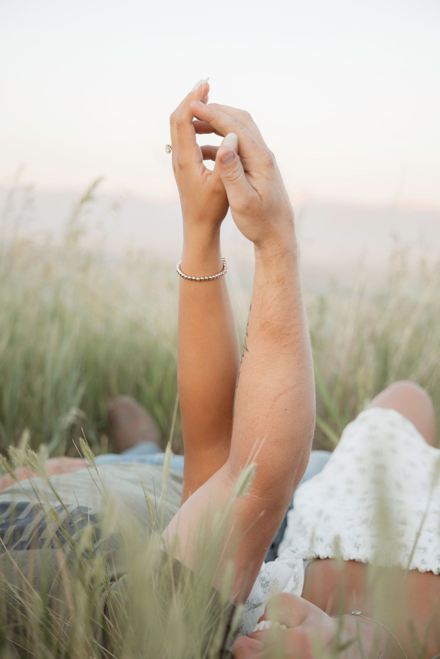 Hands raised joyfully against a soft focus background of tall grass at sunset.