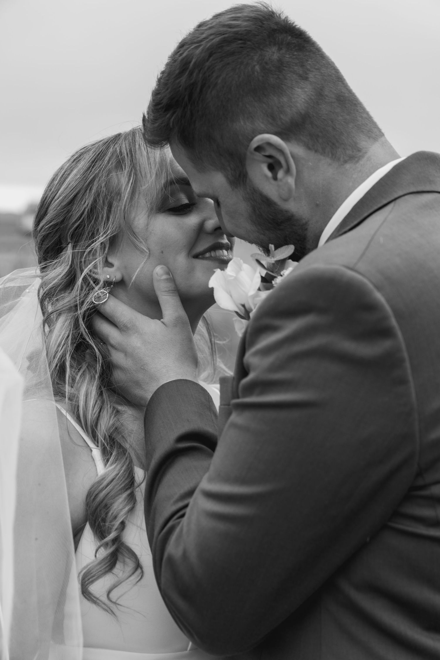 Black and white wedding photo of bride and groom sharing a tender moment, groom gently holding bride's face.