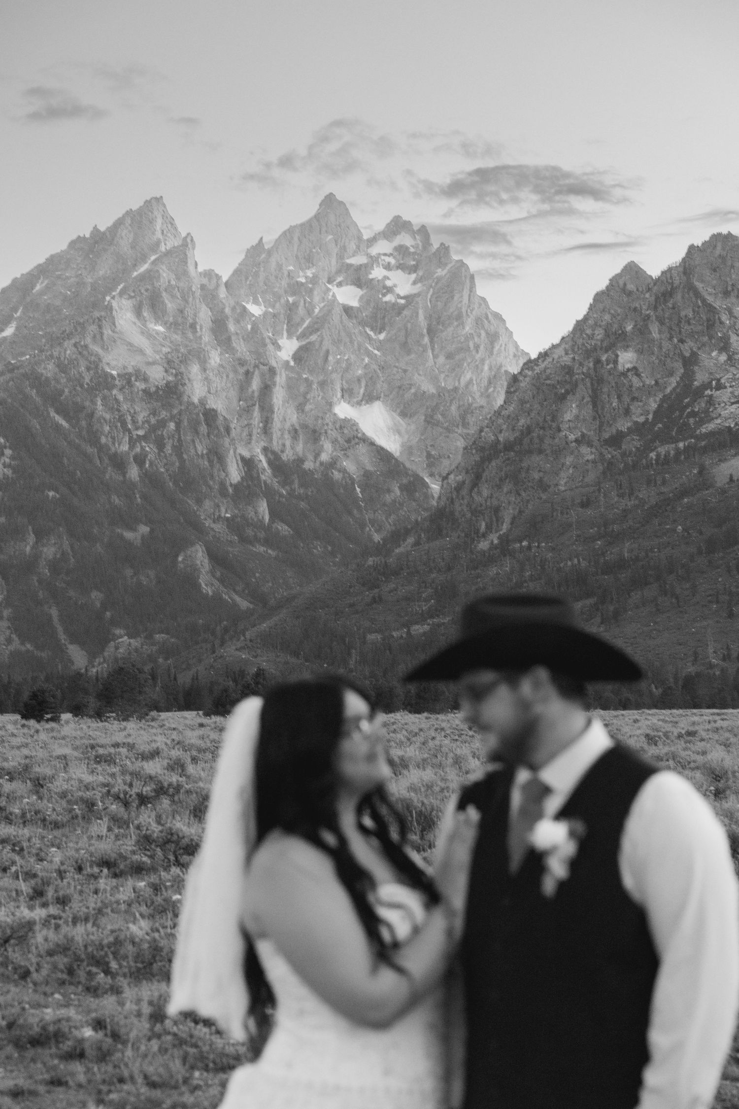 Black and white wedding photo of couple in cowboy hat and veil with Grand Teton mountains backdrop.