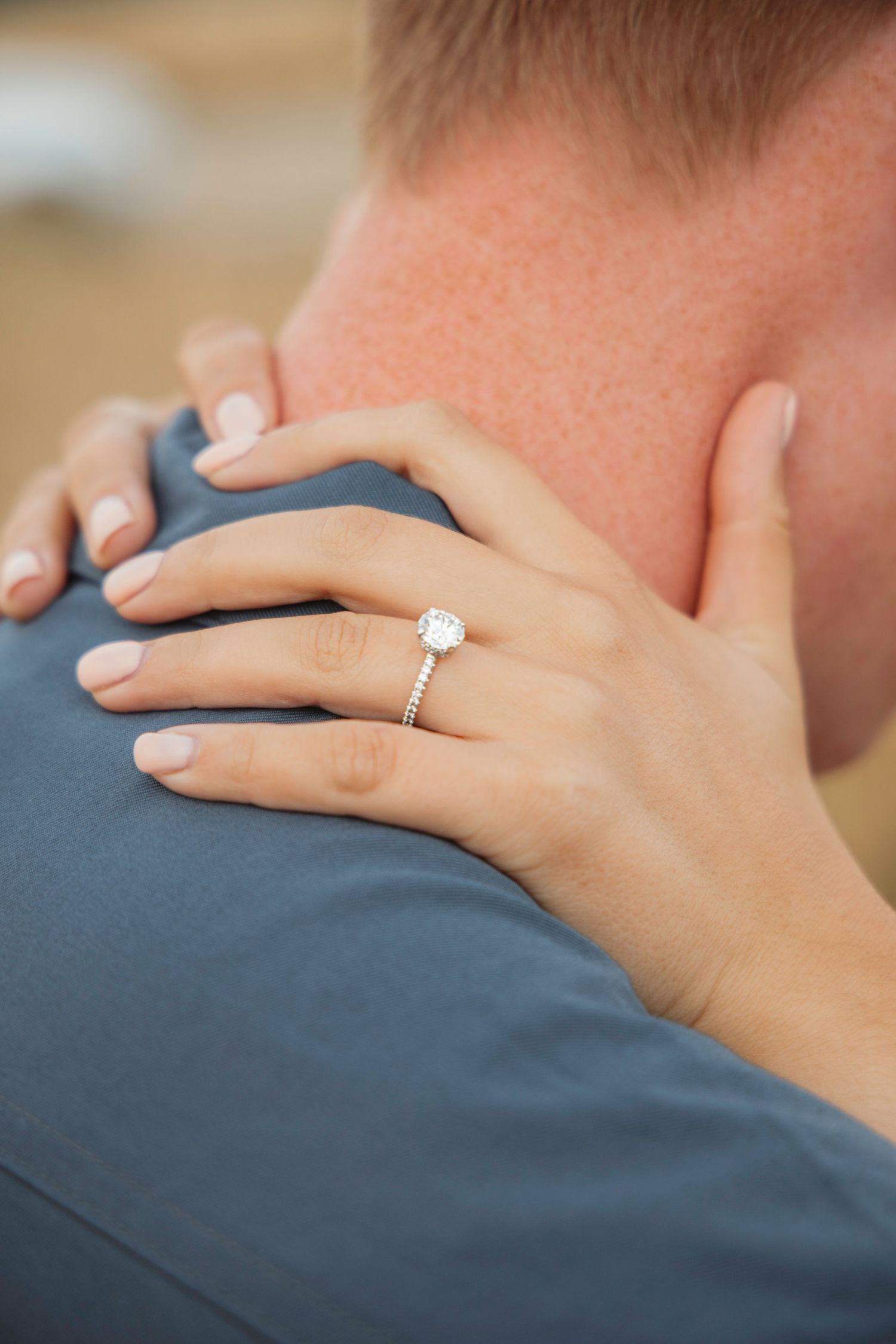 Close-up of hands showing an engagement ring against a gray background.