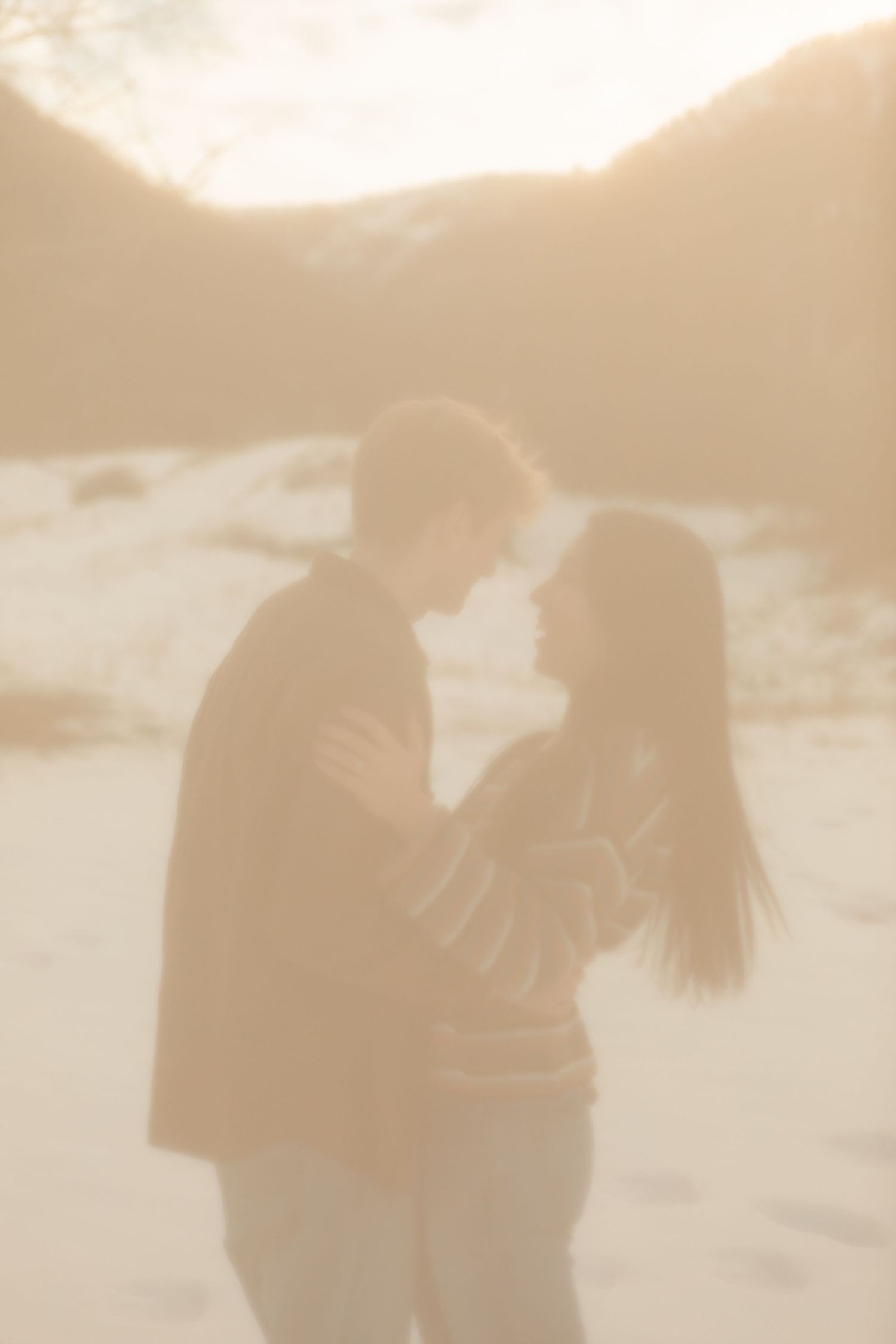 Silhouettes of a couple embracing during sunset on a beach with warm golden lighting.