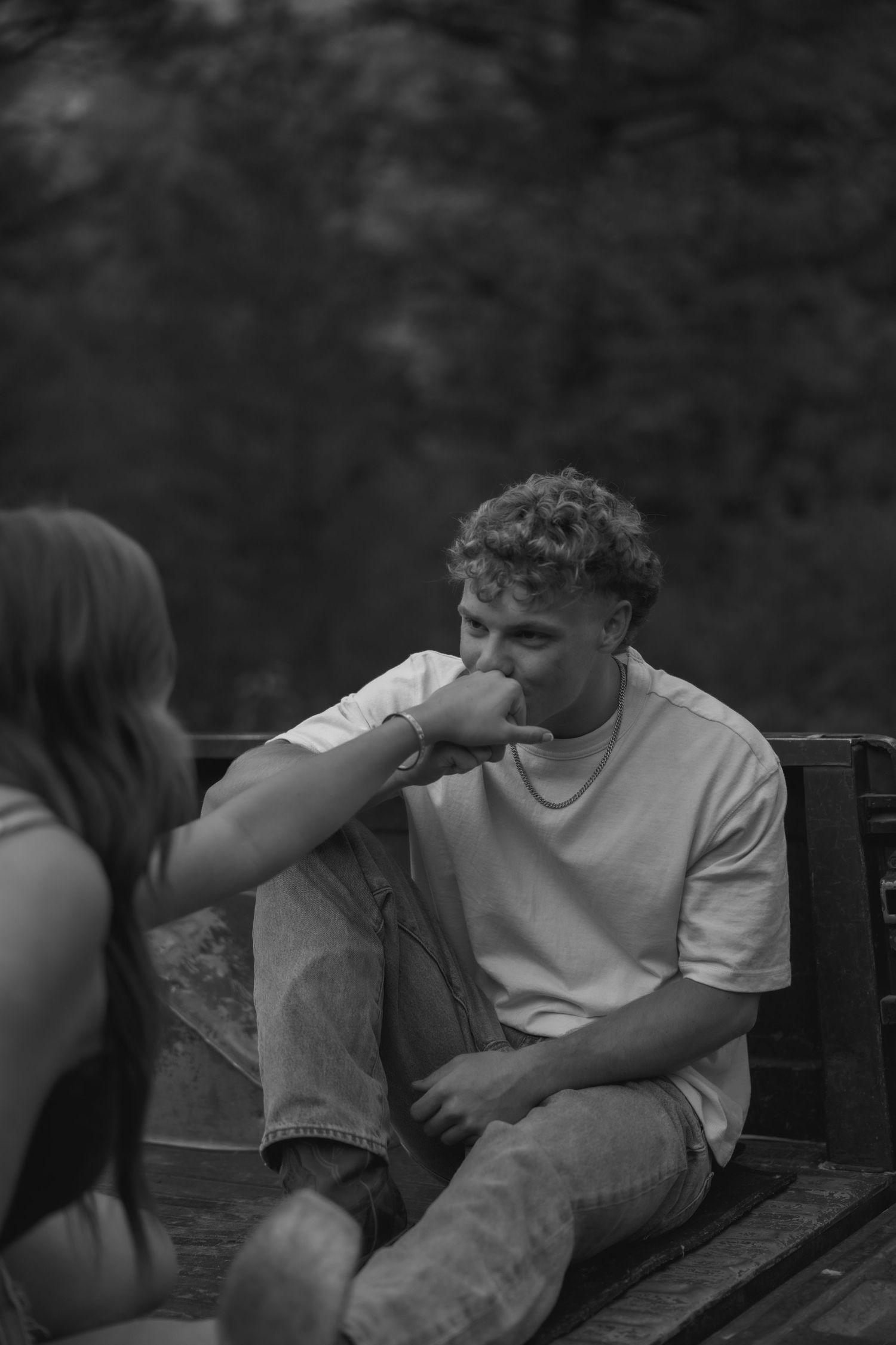 Black and white photo of a young man kissing a woman's hand while sitting outdoors on a wooden bench.