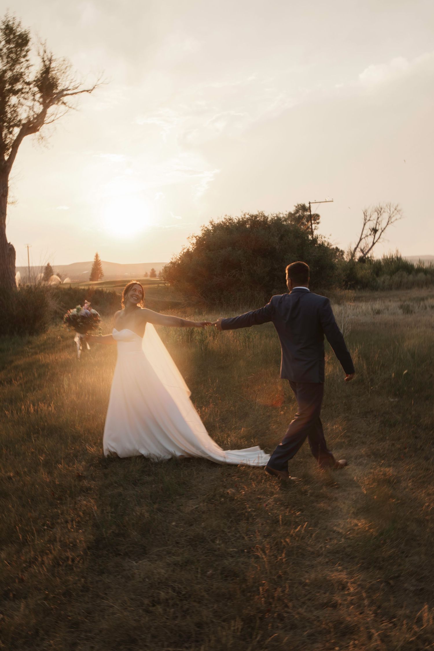 Wedding couple walking through a field at sunset with flowing dress.