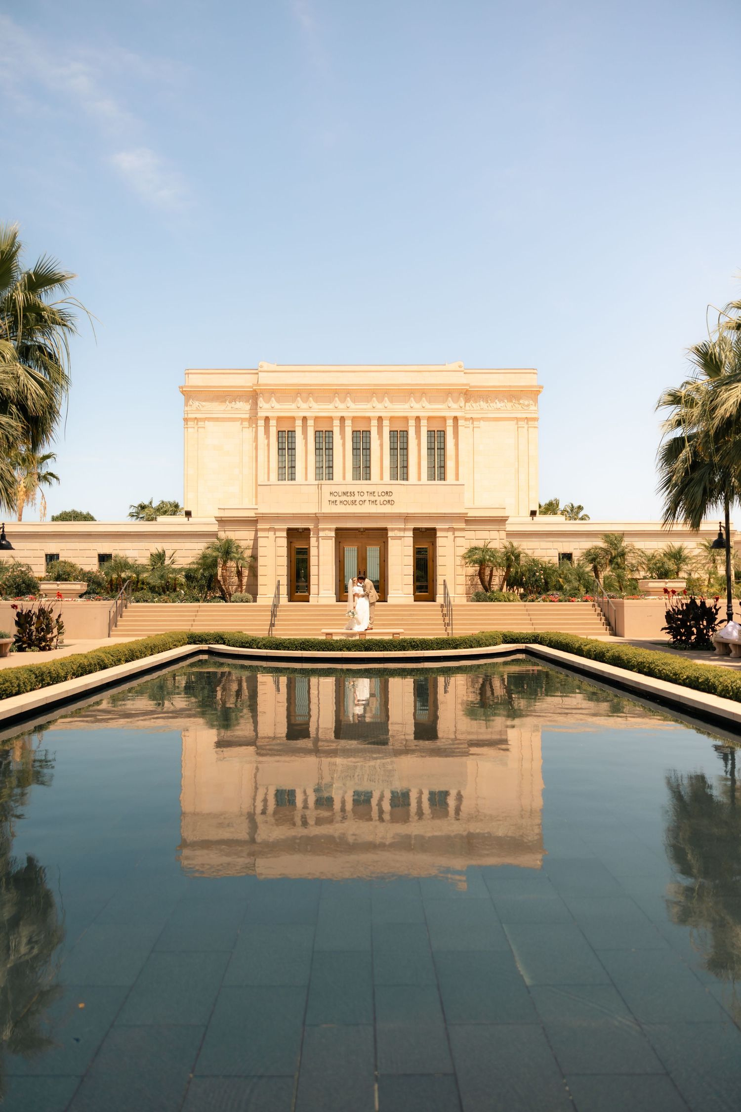 Mesa Arizona LDS Temple with reflection pool and palm trees under clear blue sky at sunset.