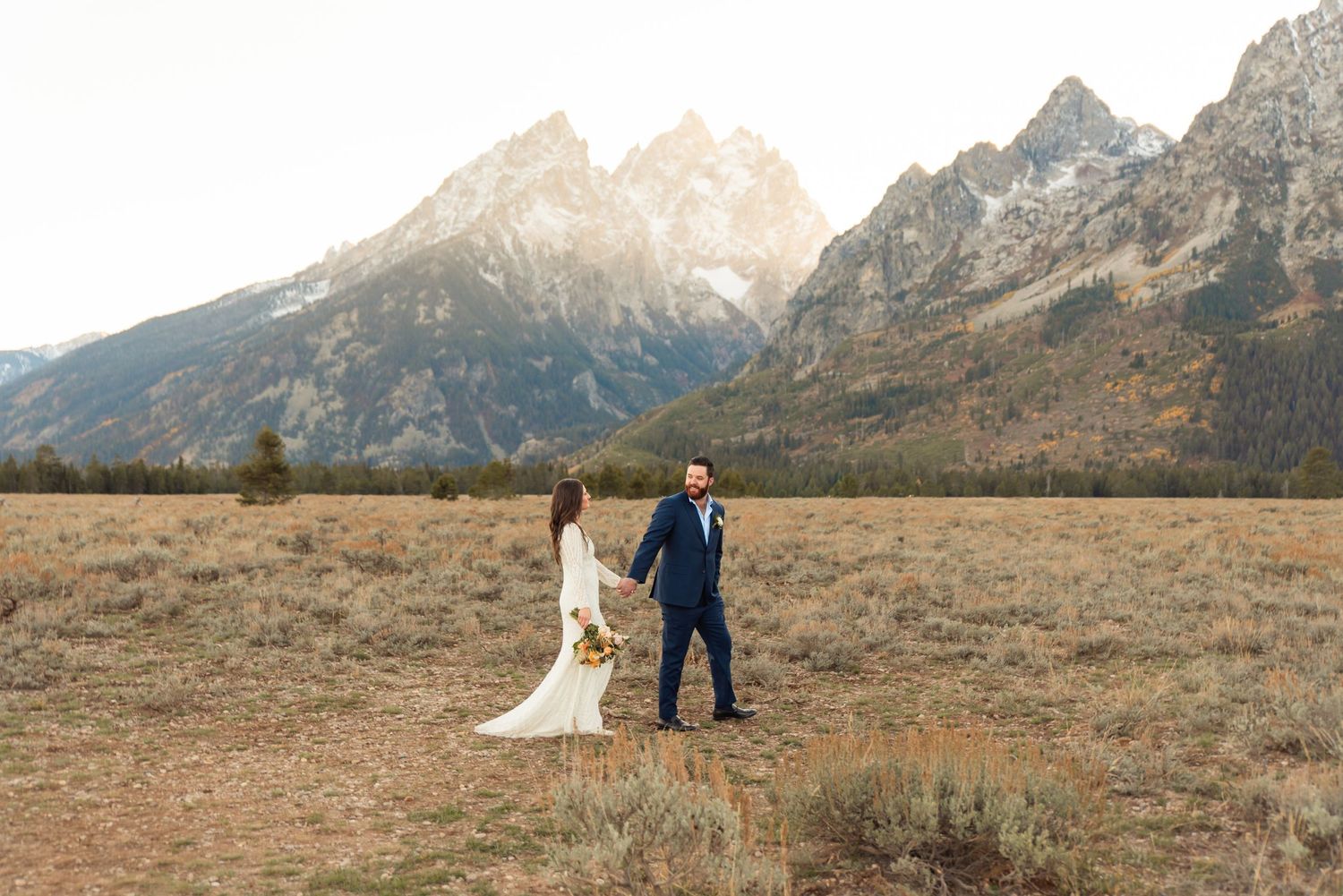 A couple stands against a dramatic mountain backdrop in a rugged landscape.