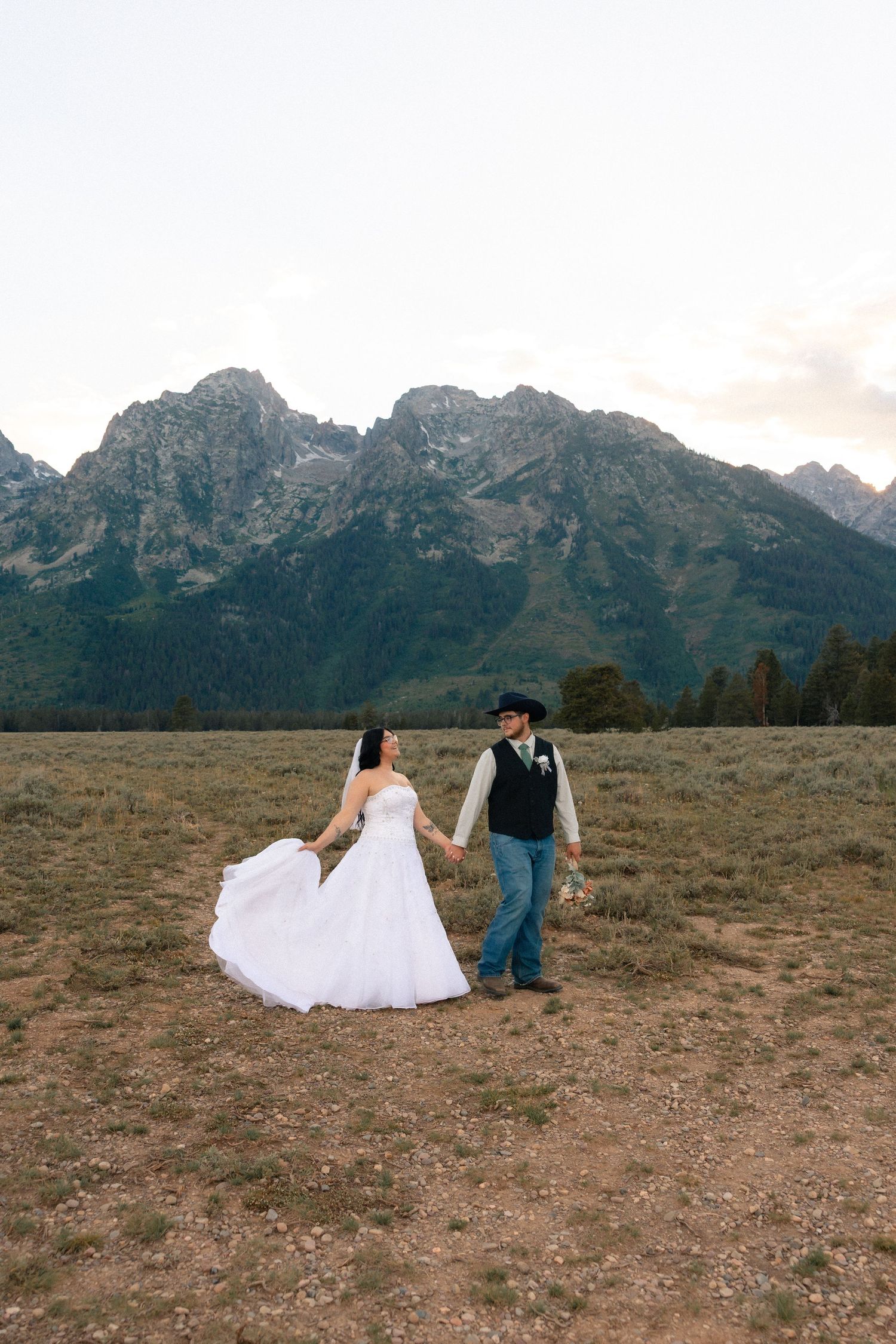 Bride and groom hold hands in a mountain meadow, with the Grand Tetons as a stunning backdrop on their wedding day.