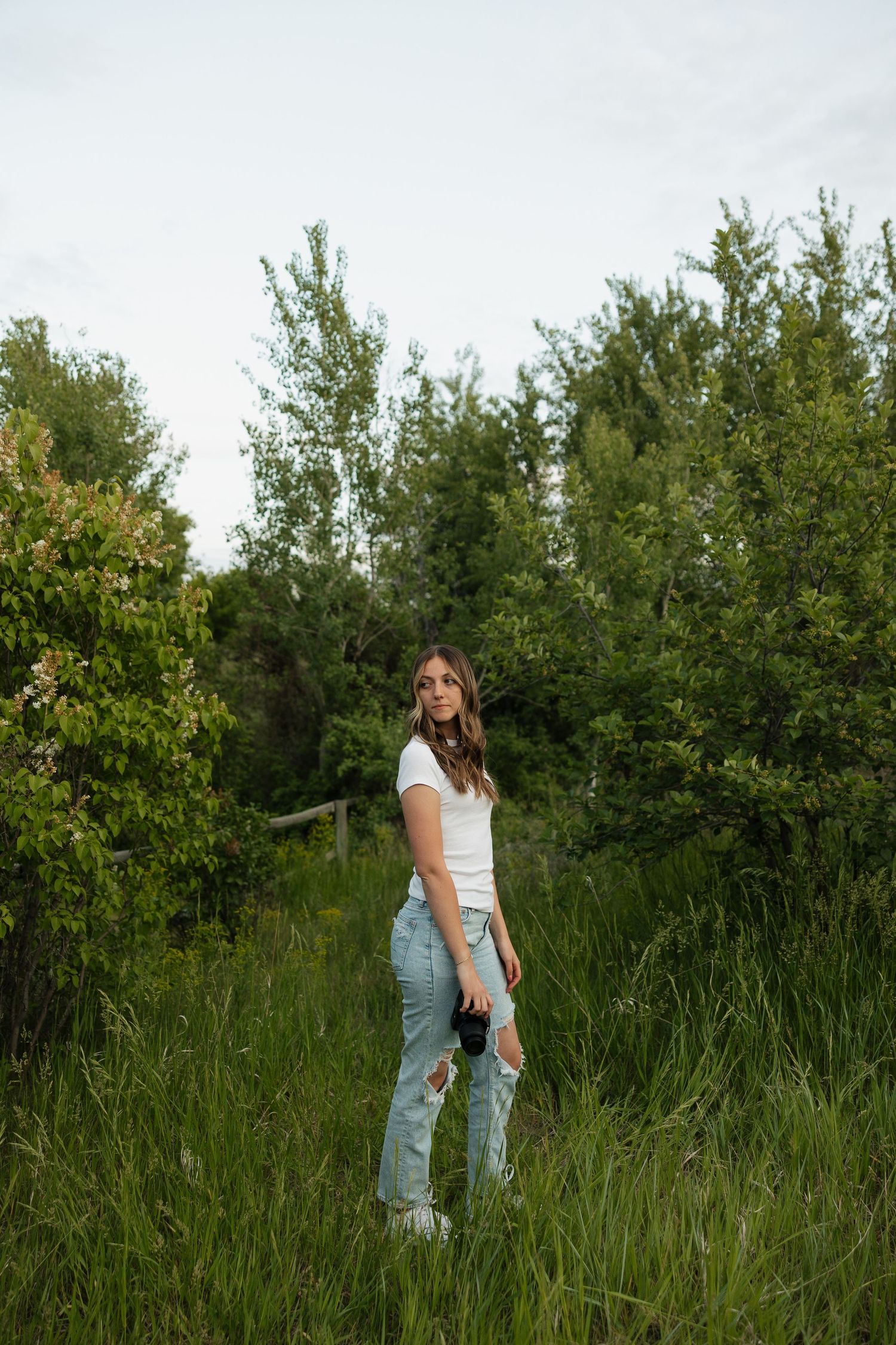 A casual portrait session in a field with tall grass and trees in the background.