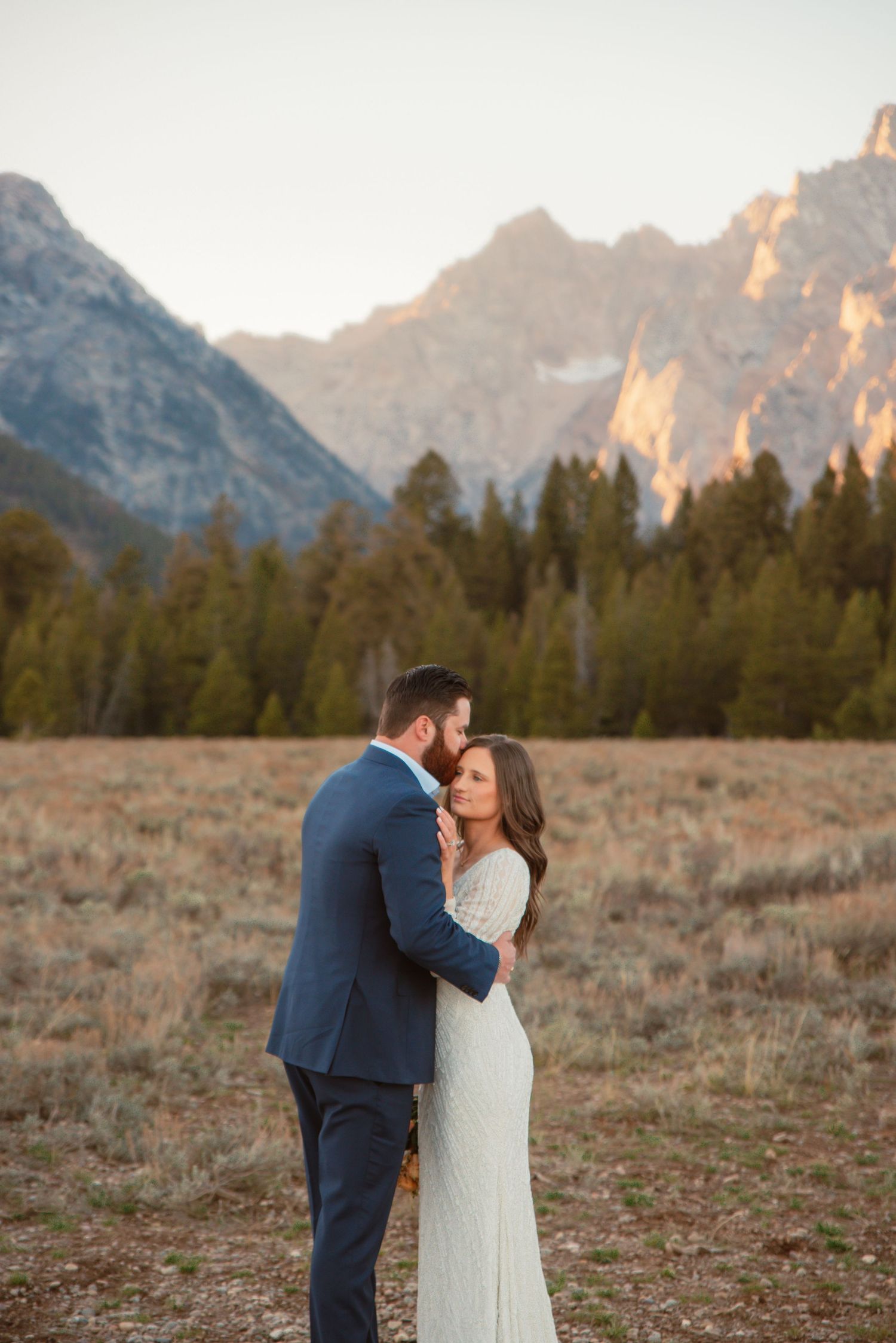 Couple sharing intimate moment against backdrop of Grand Teton mountains during sunset.