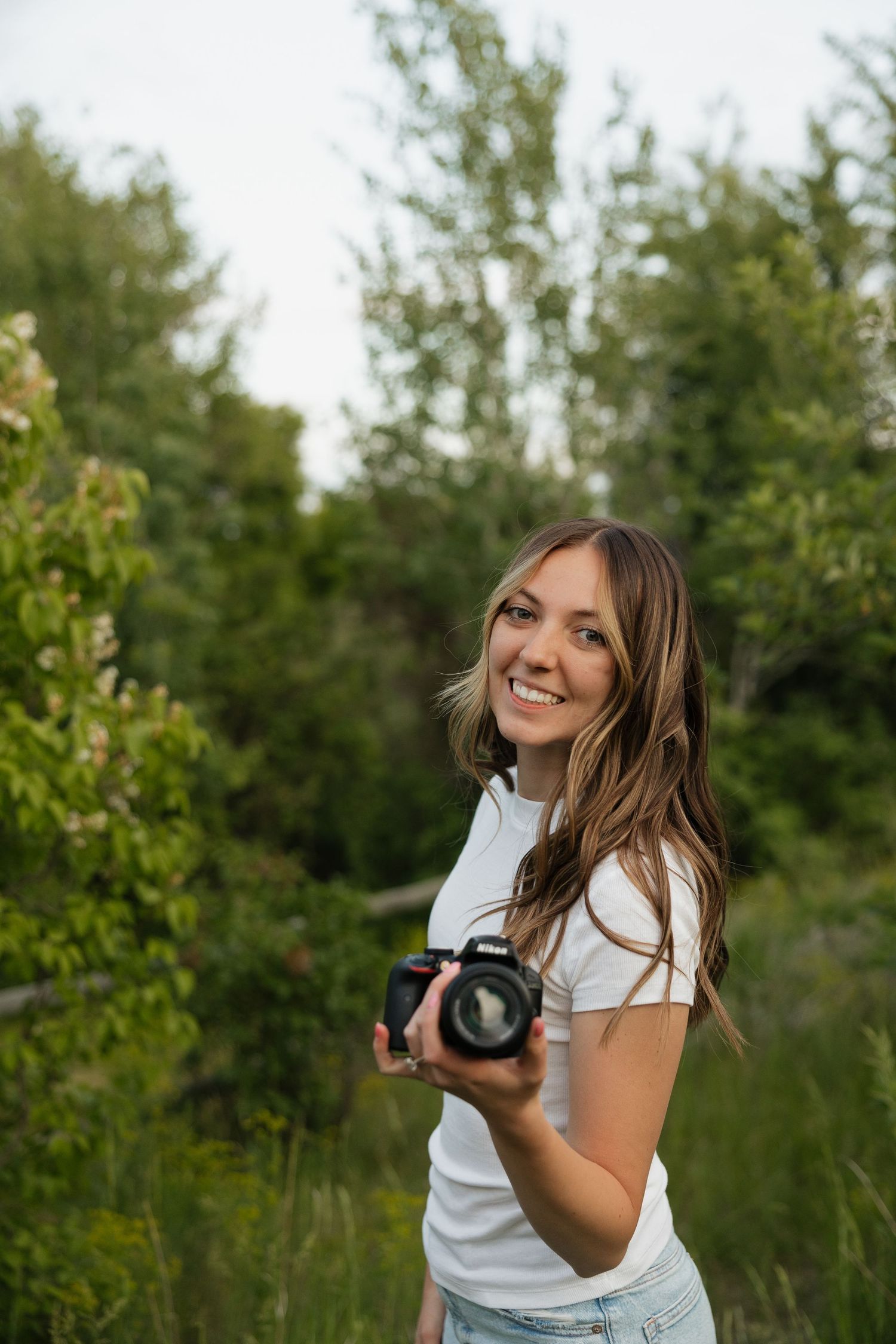 Photographer with professional camera smiling in natural outdoor setting.