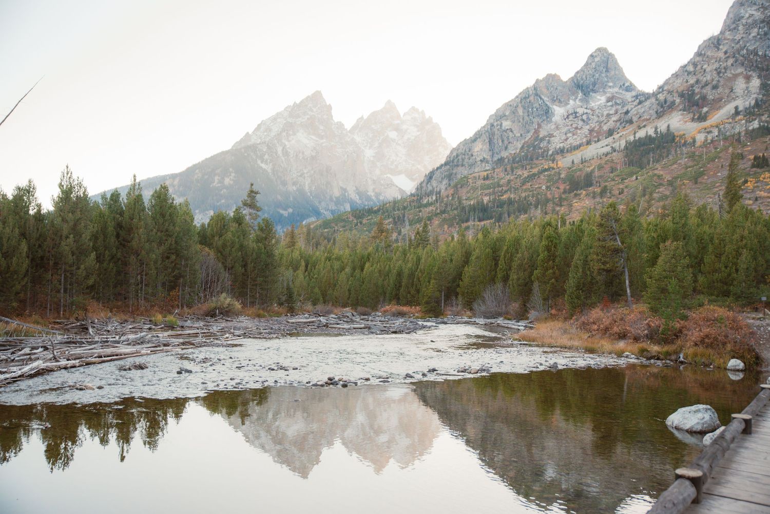 Serene mountain lake reflection with snow-capped peaks and evergreen forest.