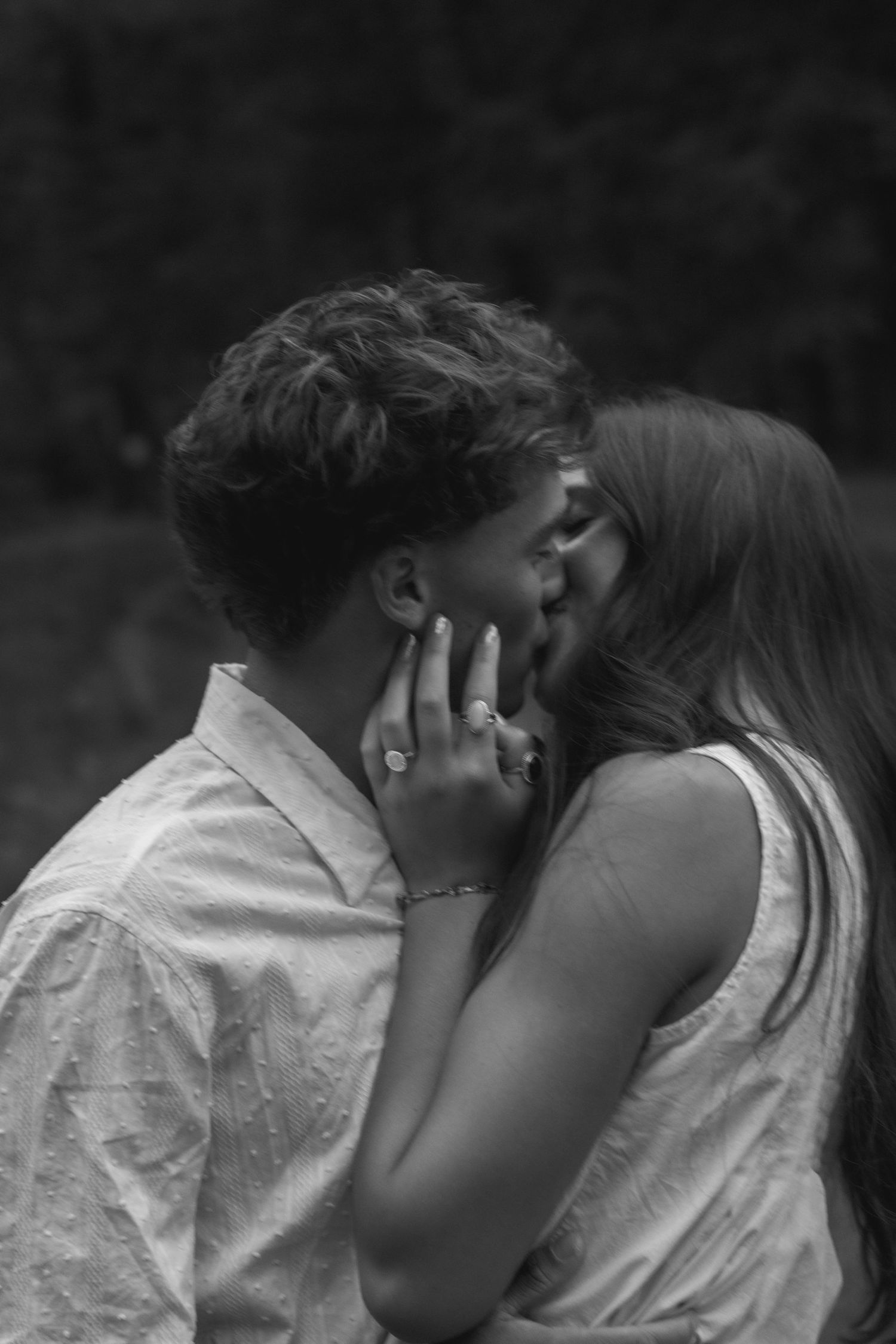 Black and white photo of a couple sharing a romantic kiss outdoors, woman wearing rings and bracelet.