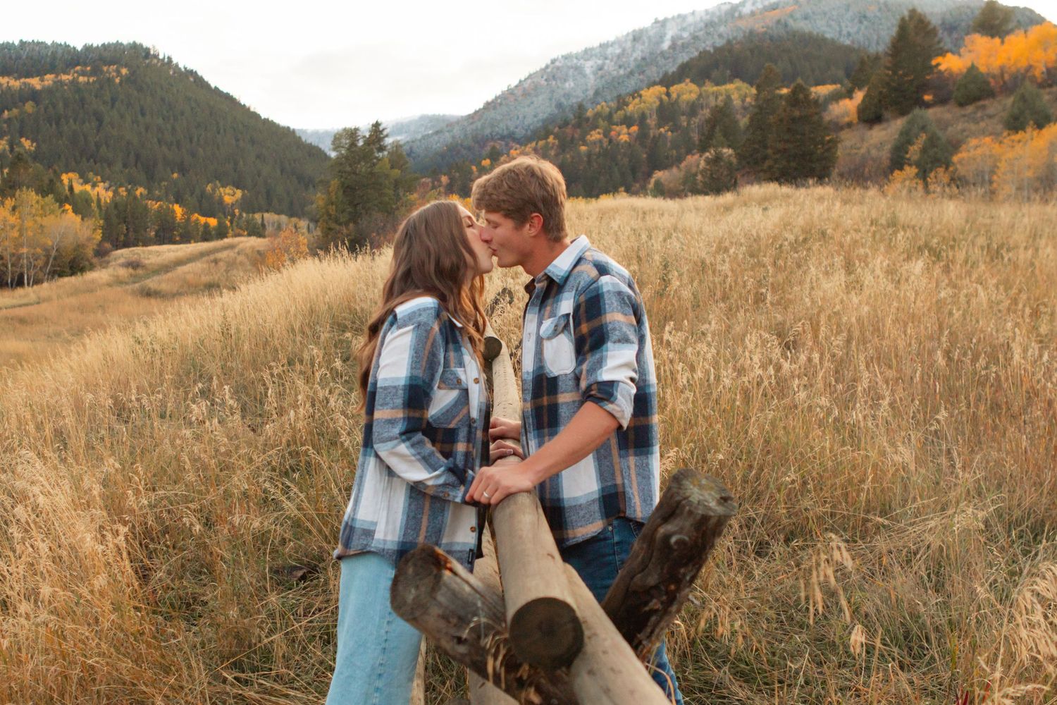 A couple embraces in a golden field during sunset with mountains in the background.