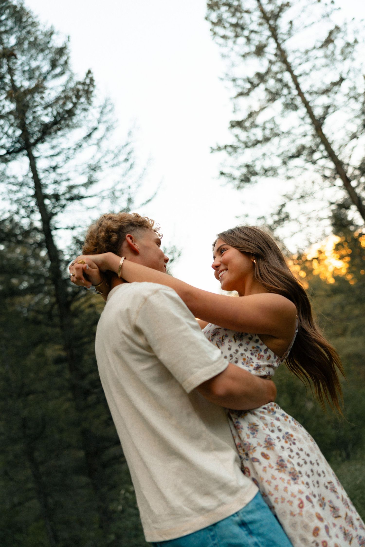 A happy couple embracing and smiling at each other in a forest at golden hour sunset.