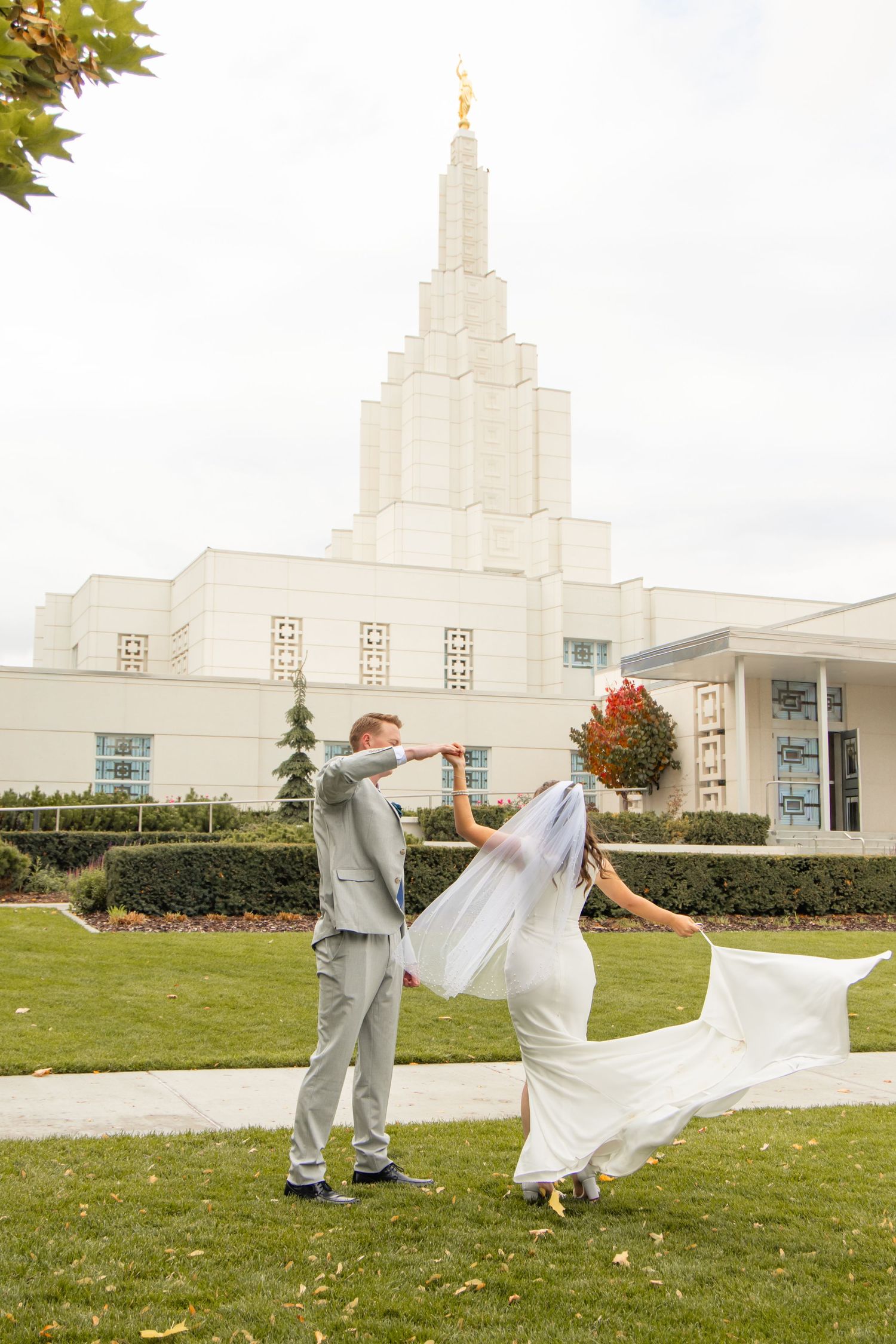 A playful couple dances and spins on a grassy lawn in front of a white temple building.