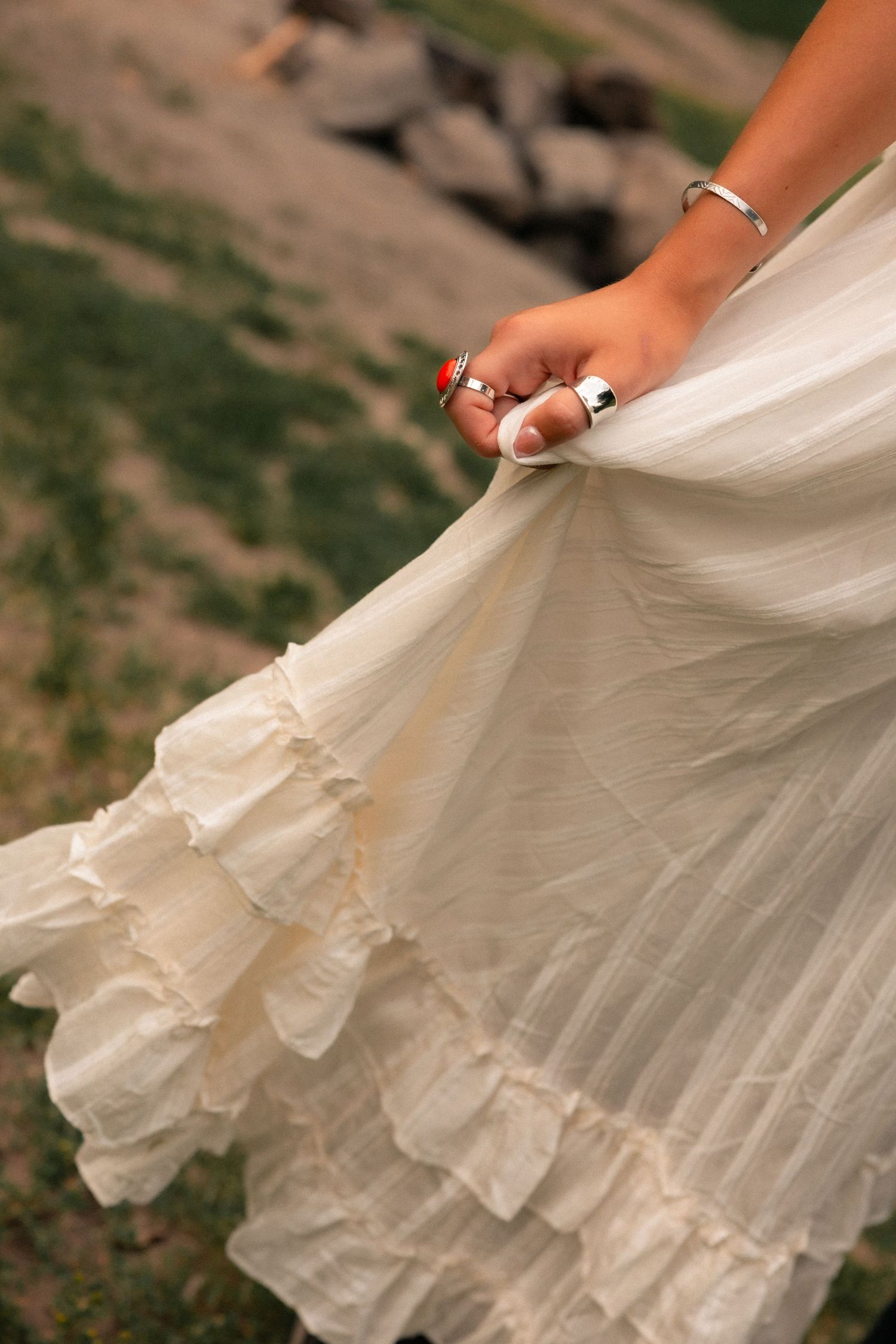 Close-up of a woman's hand holding a flowing white ruffled skirt outdoors.