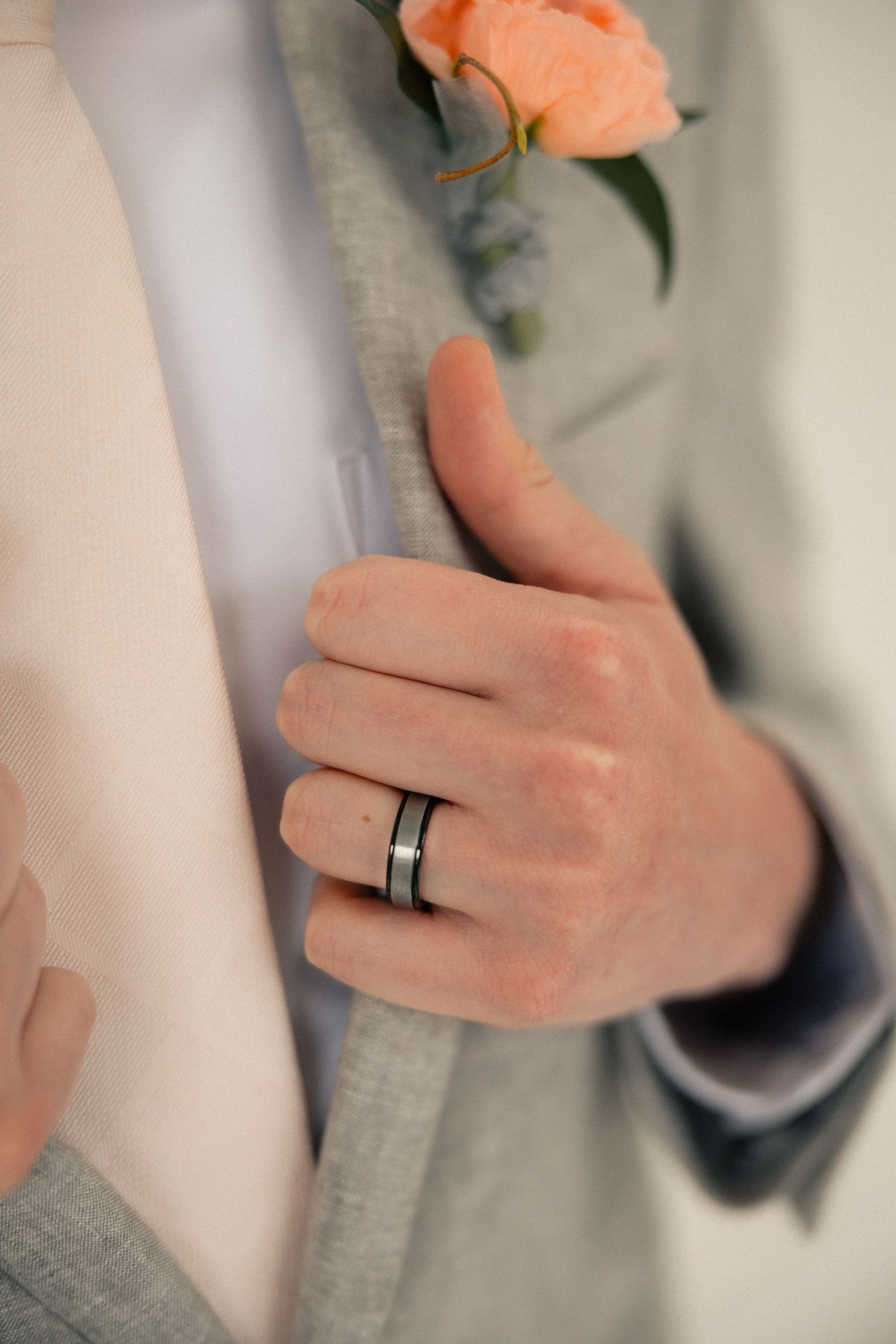 Close-up of groom's hand wearing a black and silver wedding band, resting on bride's waist at wedding.