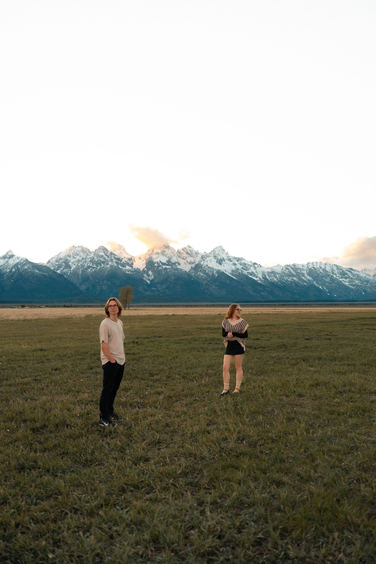 Two women standing in a green field with snow-capped Grand Teton mountains at dusk.