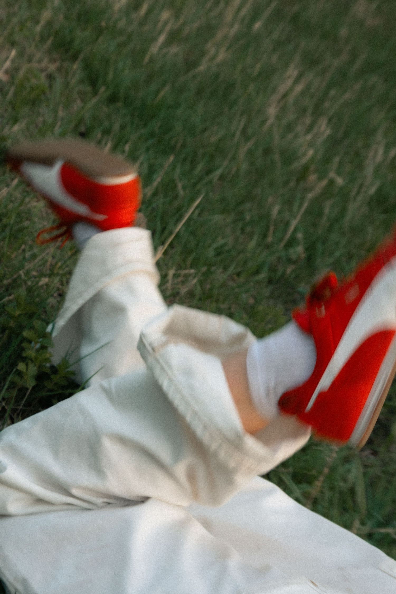 Person wearing white pants and red sneakers lying on green grass in a dynamic motion blur shot.