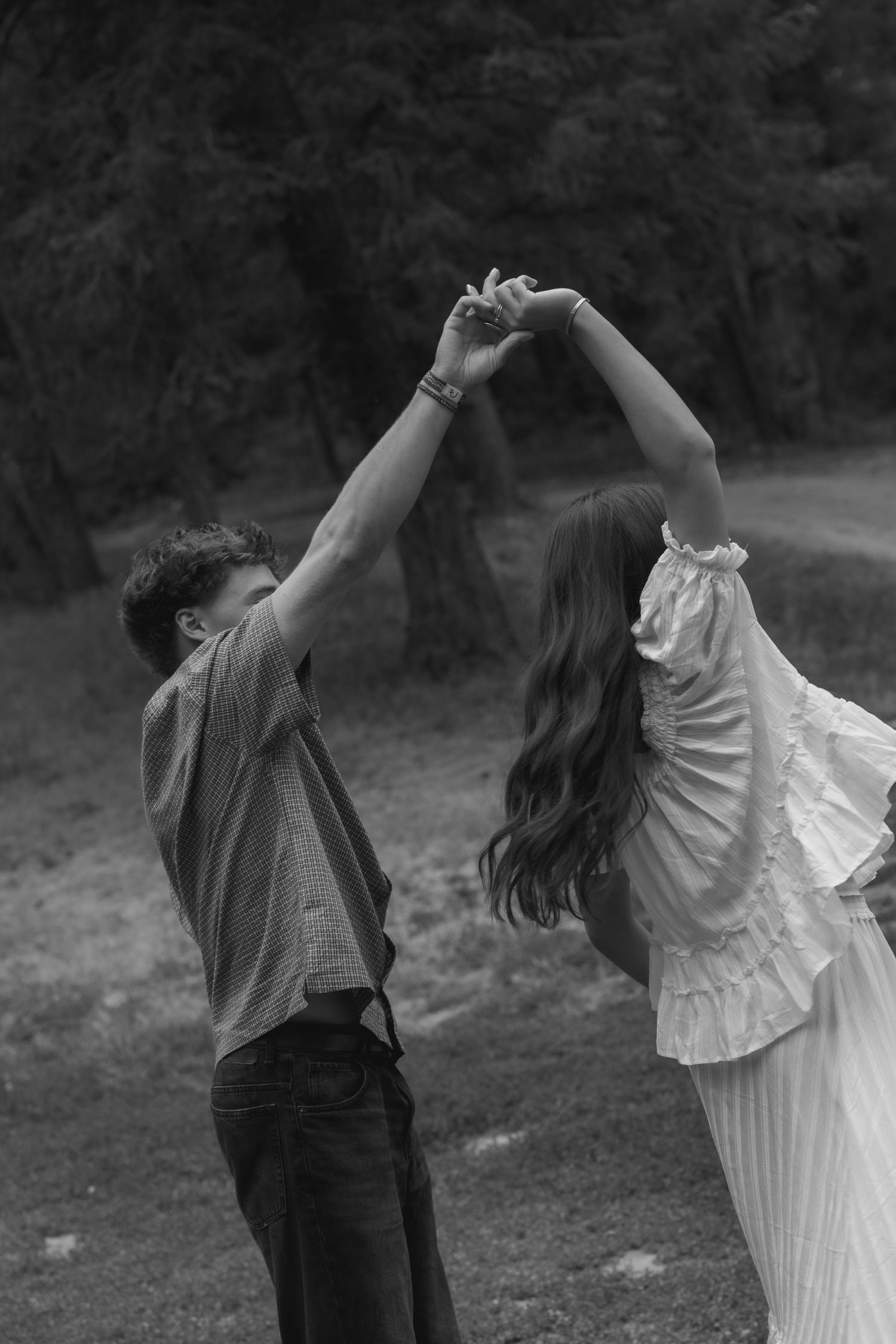 Black and white photo of a couple dancing outdoors, raising their joined hands together in a romantic moment.