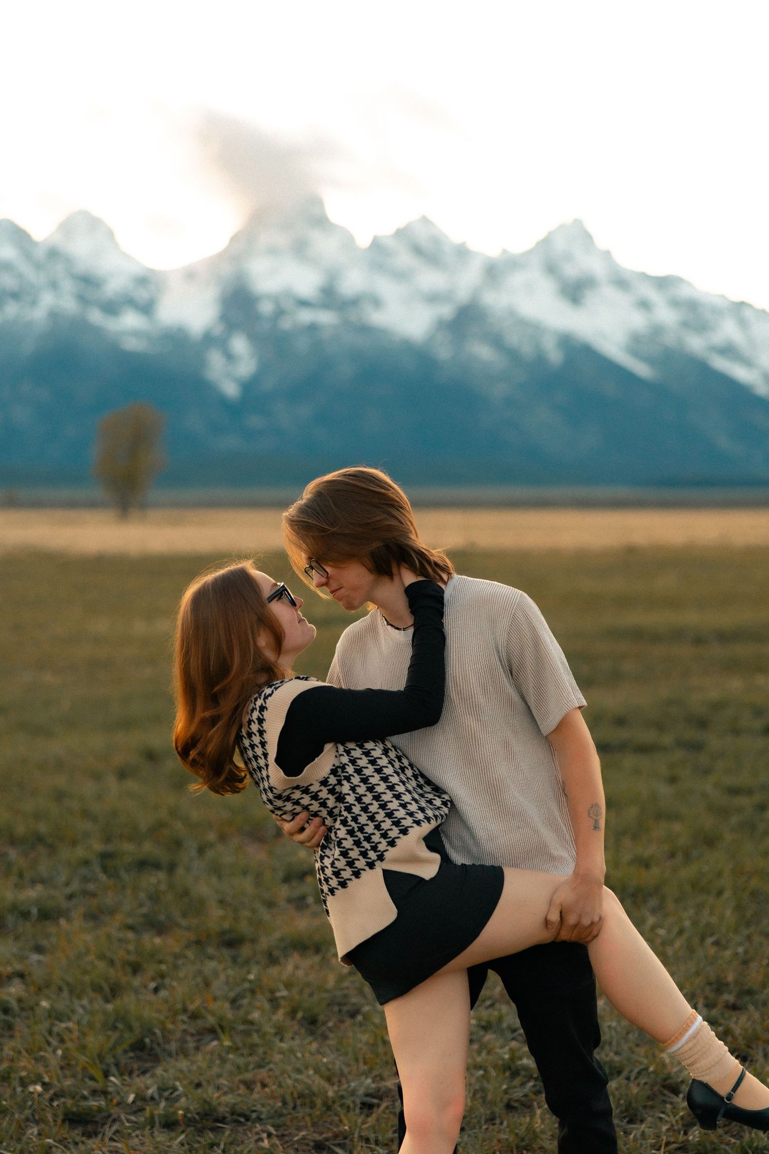 A couple embracing romantically in a field with Grand Teton mountains at sunset.