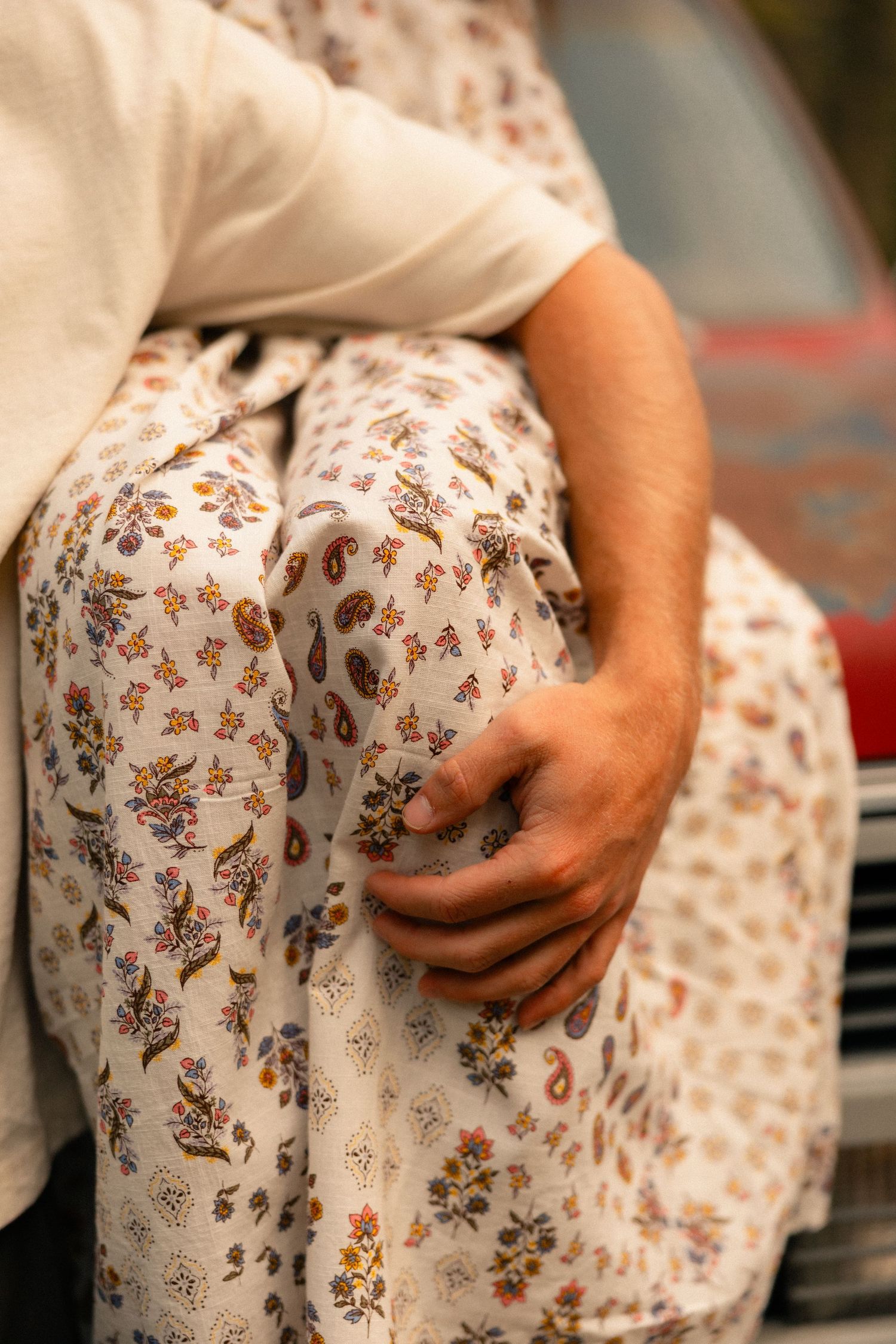 A man gently holds a woman's hand on her floral dress while sitting on a red vehicle.