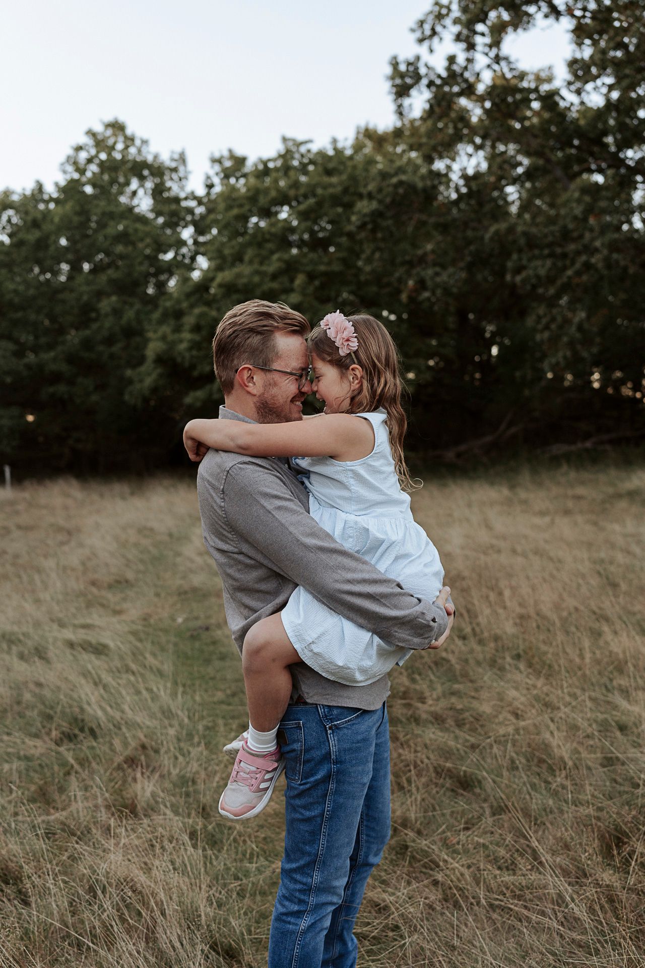 En pappa håller sin dotter i famnen, de gnuggar varandras näsa. I en härlig miljö med ängar och grönt.