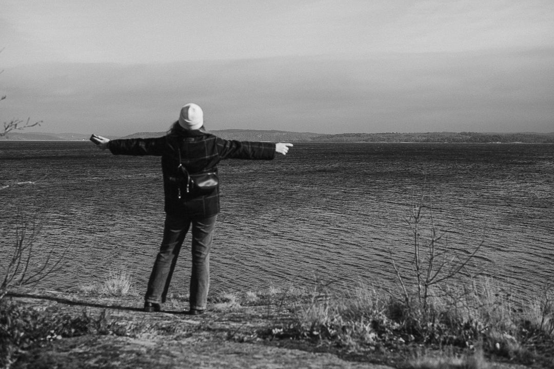Kvinna som står på ett berg vid havet, hon står med ryggen mot kameran och håller ut armarna.