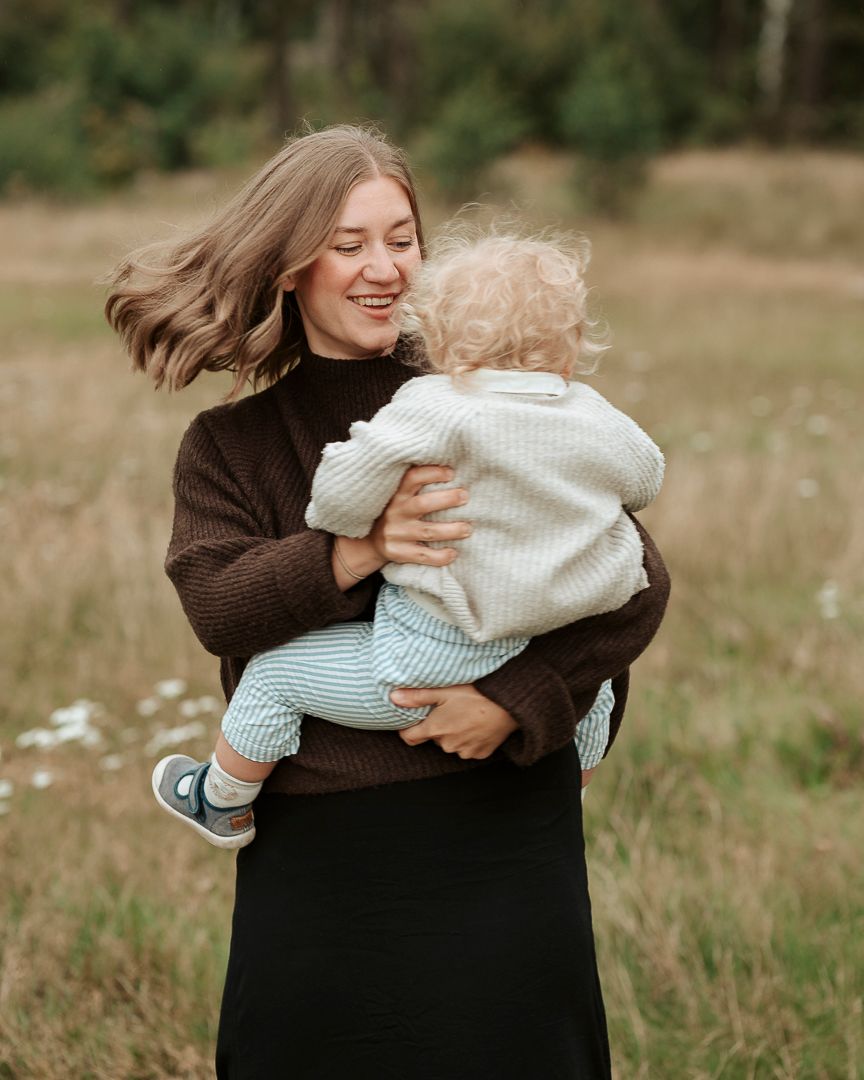 Mamma som har sitt barn i famnen, hon snurrar runt med barnet och hennes hår flyger i vinden.